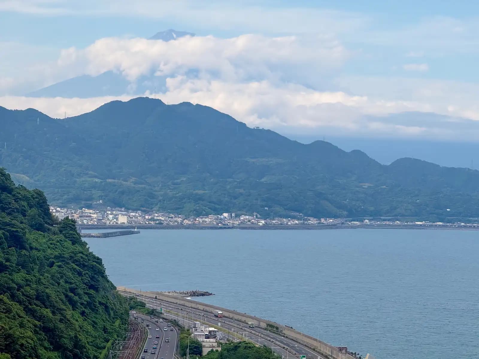 Fuji's summit above the clouds, the base of it hidden. Down below, traffic along the seawall.