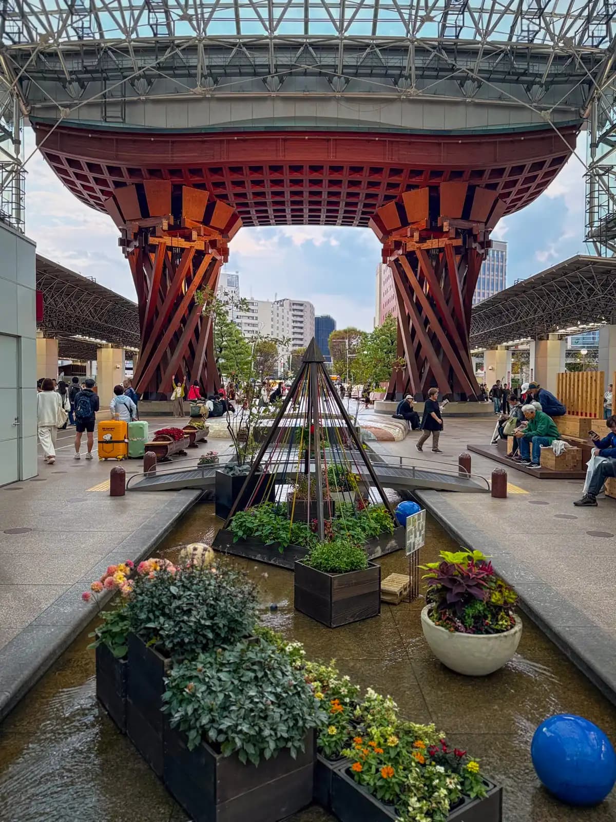 The Tsuzumi Gate at Kanazawa Station's east exit, seen from behind the flower planters in the shallow water channel. The wooden gate is shaped after a tsuzumi, a hand drum used in Noh theater.