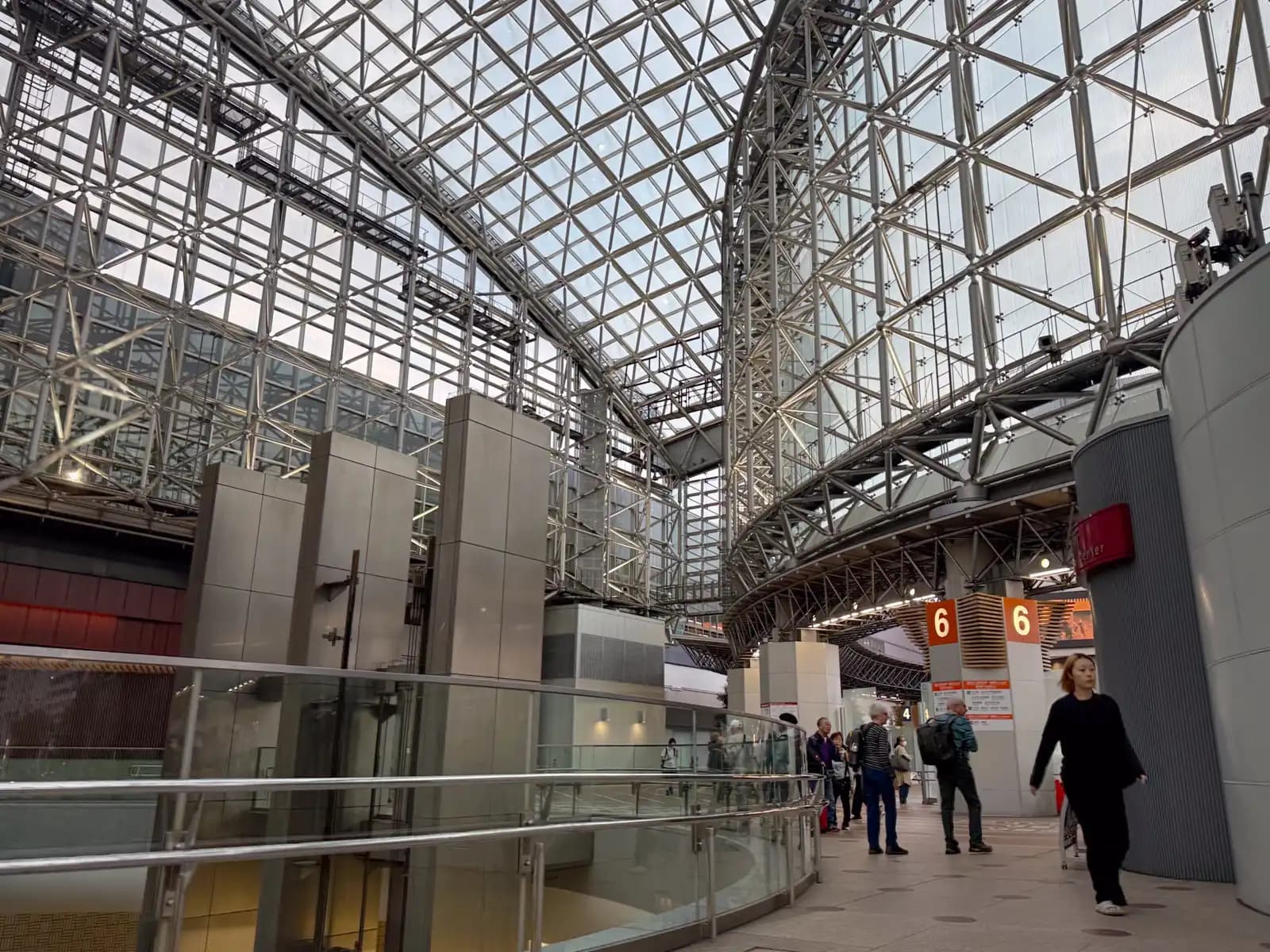 Inside the Motenashi Dome, the glass and steel roof that covers the plaza in front of Kanazawa Station. The signs for bus stop 6 are on the right.