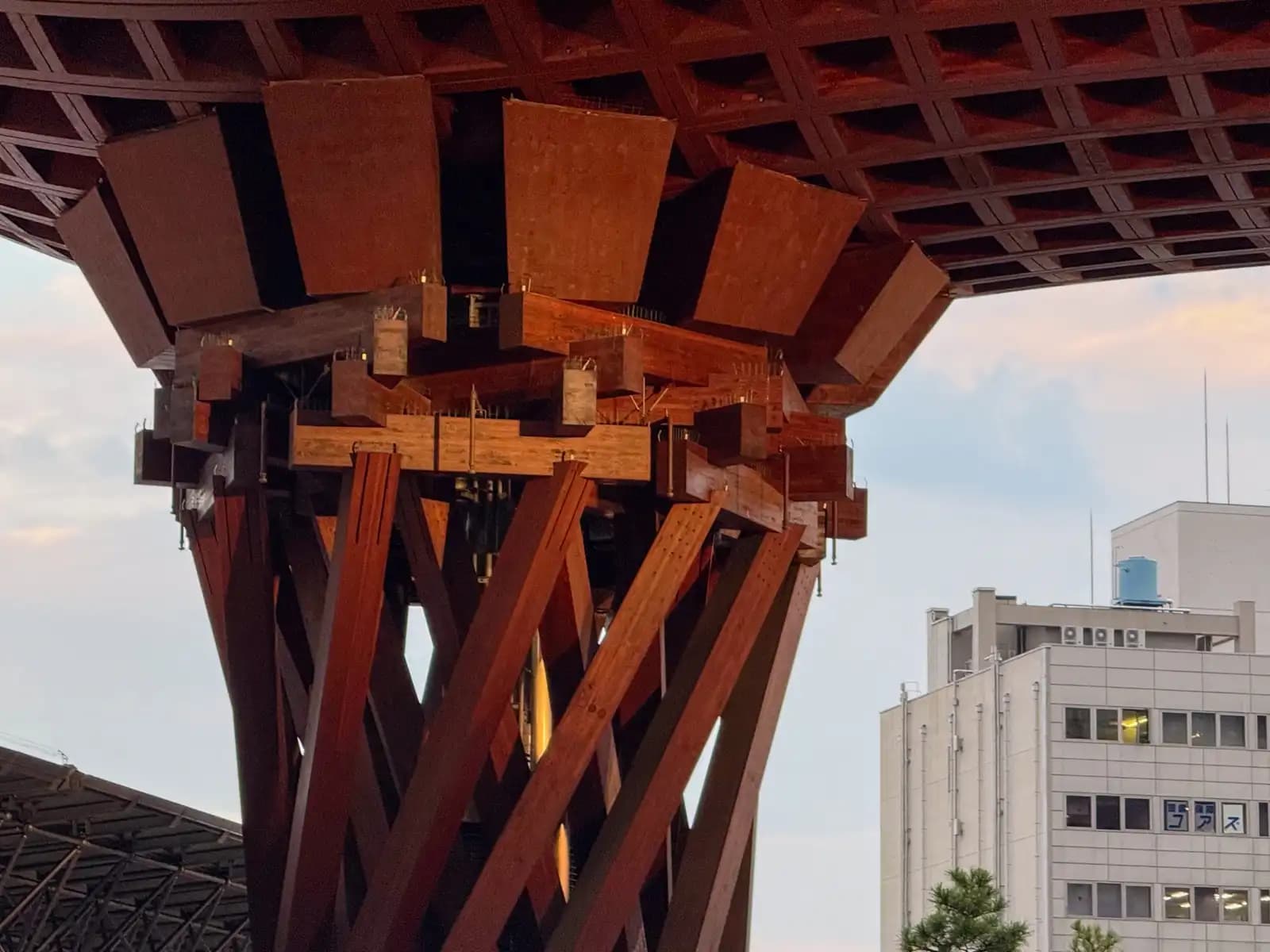 The top of one of the Tsuzumi Gate's two pillars, where the twisted wooden beams meet the roof. An office building stands to the right.