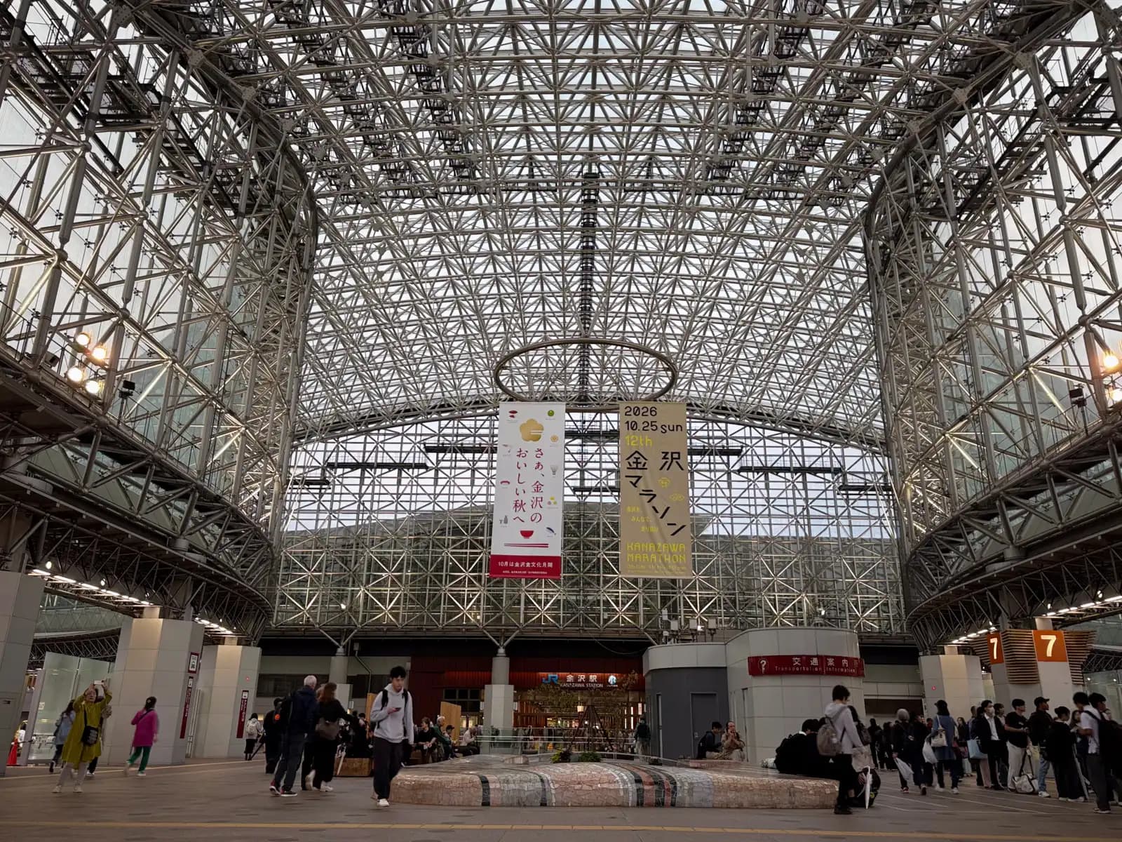 The main hall under the Motenashi Dome. Banners hanging from the roof advertise Kanazawa's autumn food and the 12th Kanazawa Marathon on October 25, 2026.