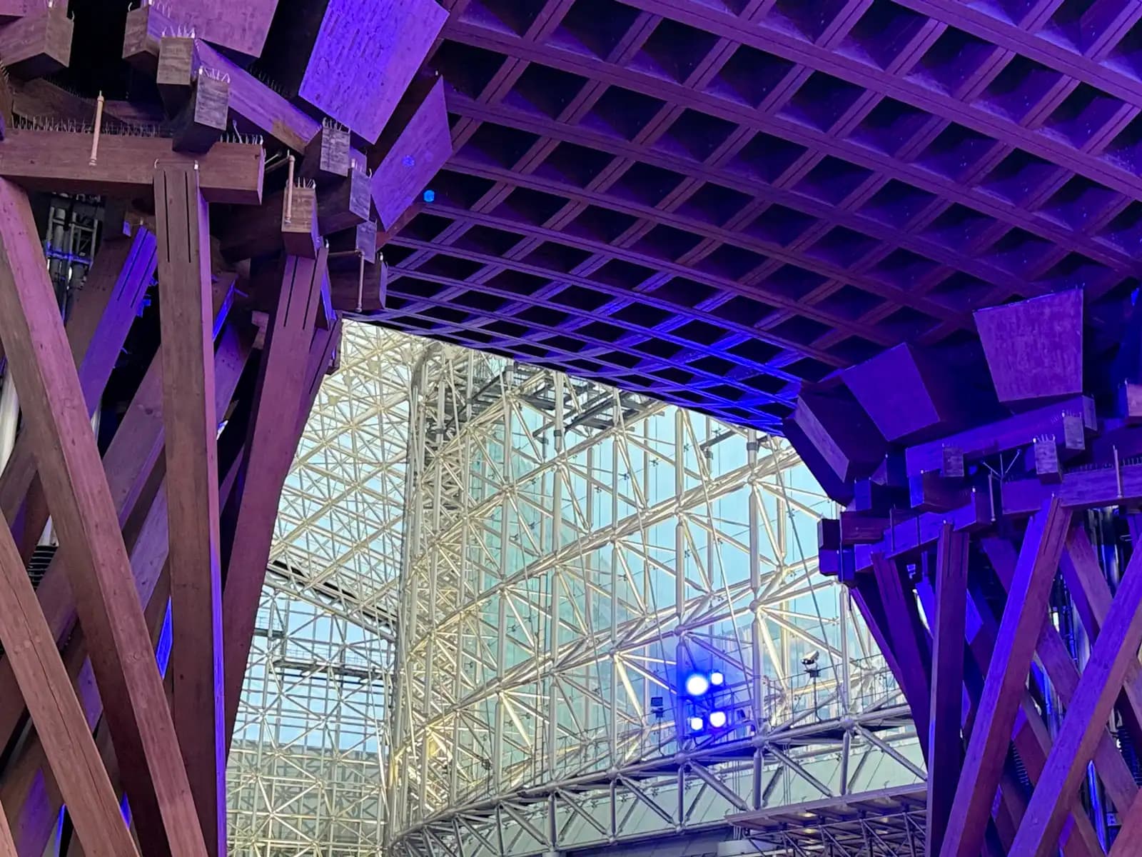 Looking up through the Tsuzumi Gate in the evening, when the wooden pillars and roof are lit in purple. The steel frame of the Motenashi Dome is behind.