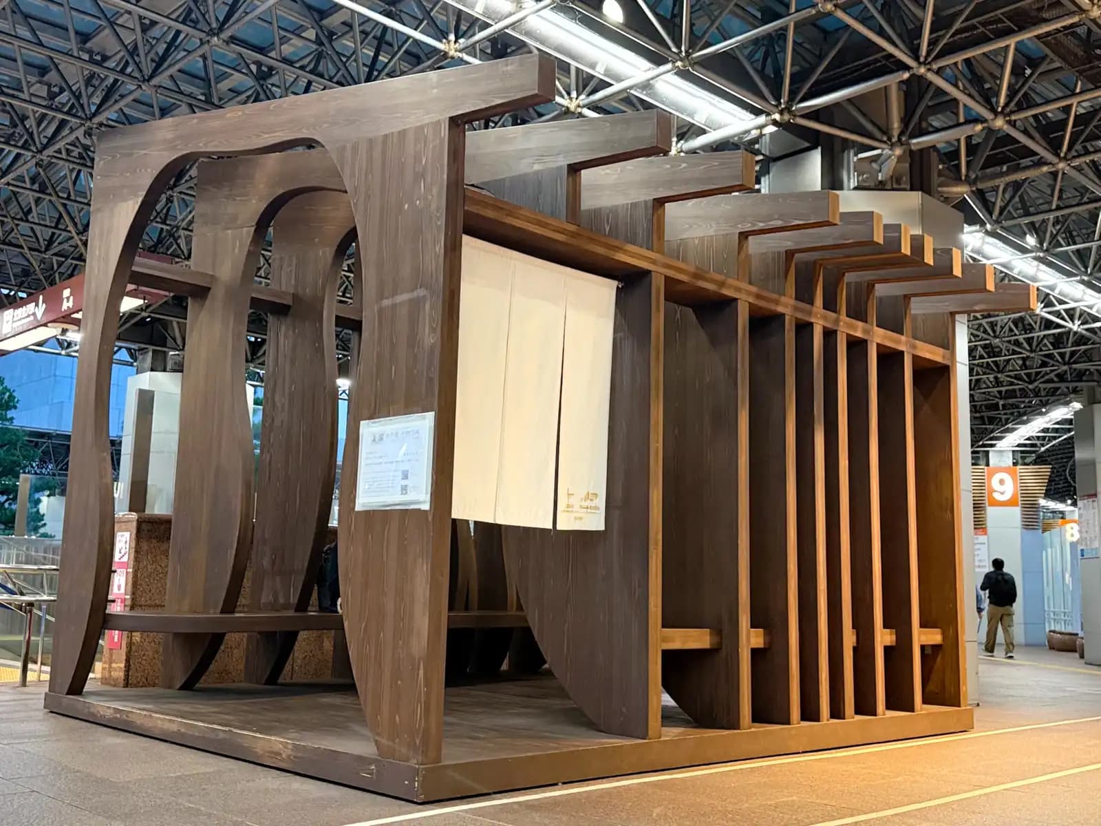 A wooden seating structure with a white noren curtain, set up in the bus terminal outside the station.