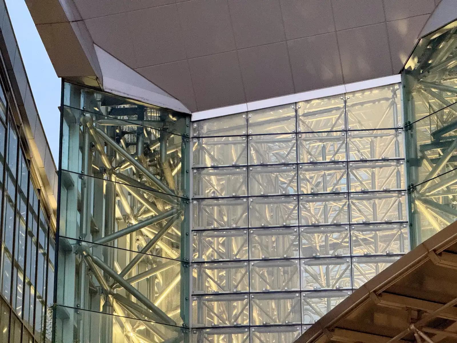 Glass walls of the station building with the steel frame visible behind the panels, lit from inside.