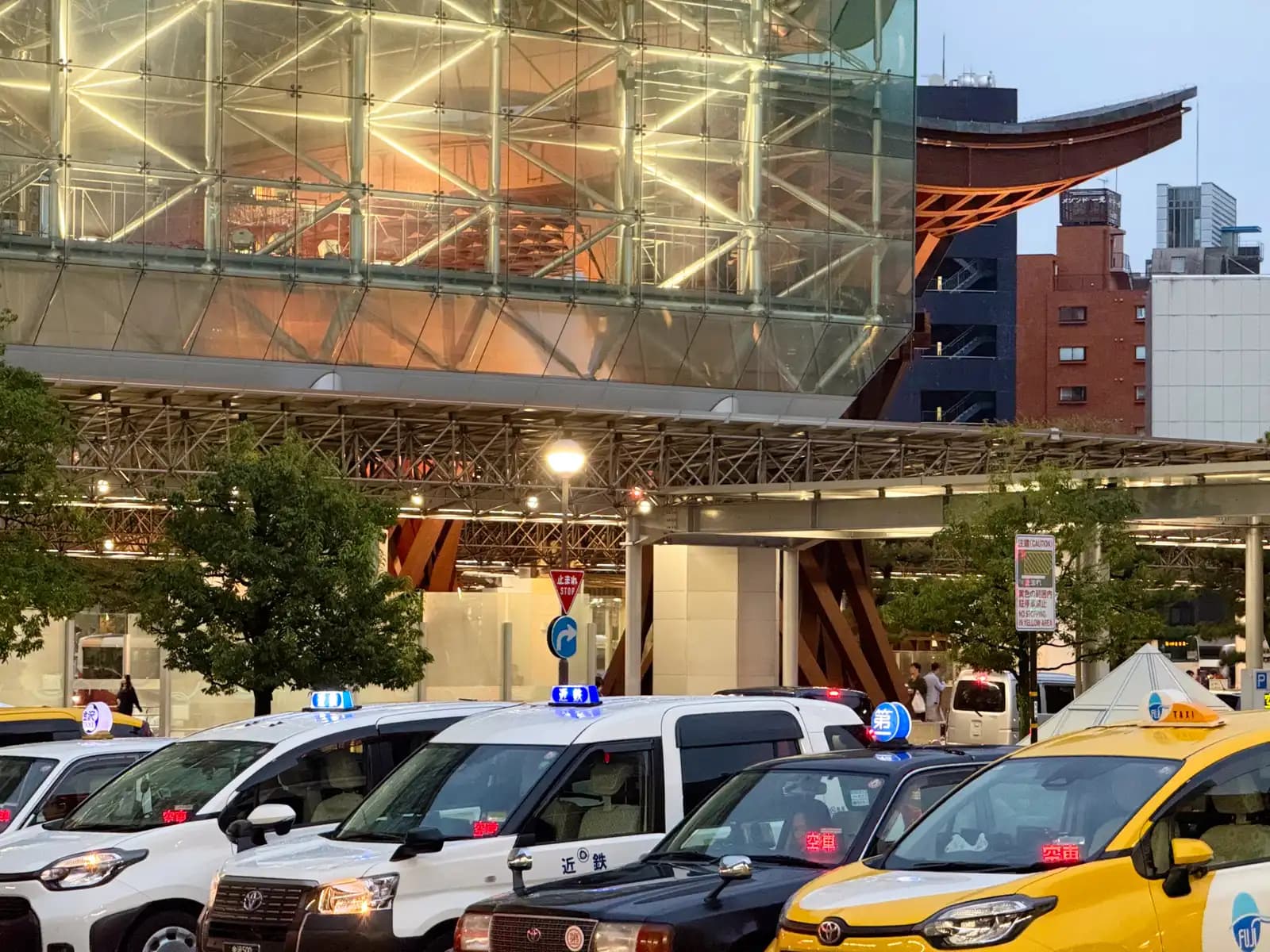 Taxis lined up at the taxi stand in front of the station in the evening, with the Motenashi Dome and the roof of the Tsuzumi Gate behind.