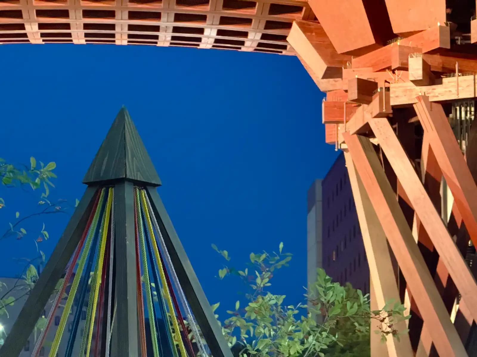 The wooden pyramid with colored cords that stands in the water channel by the Tsuzumi Gate, against the evening sky. One of the gate's pillars is on the right.