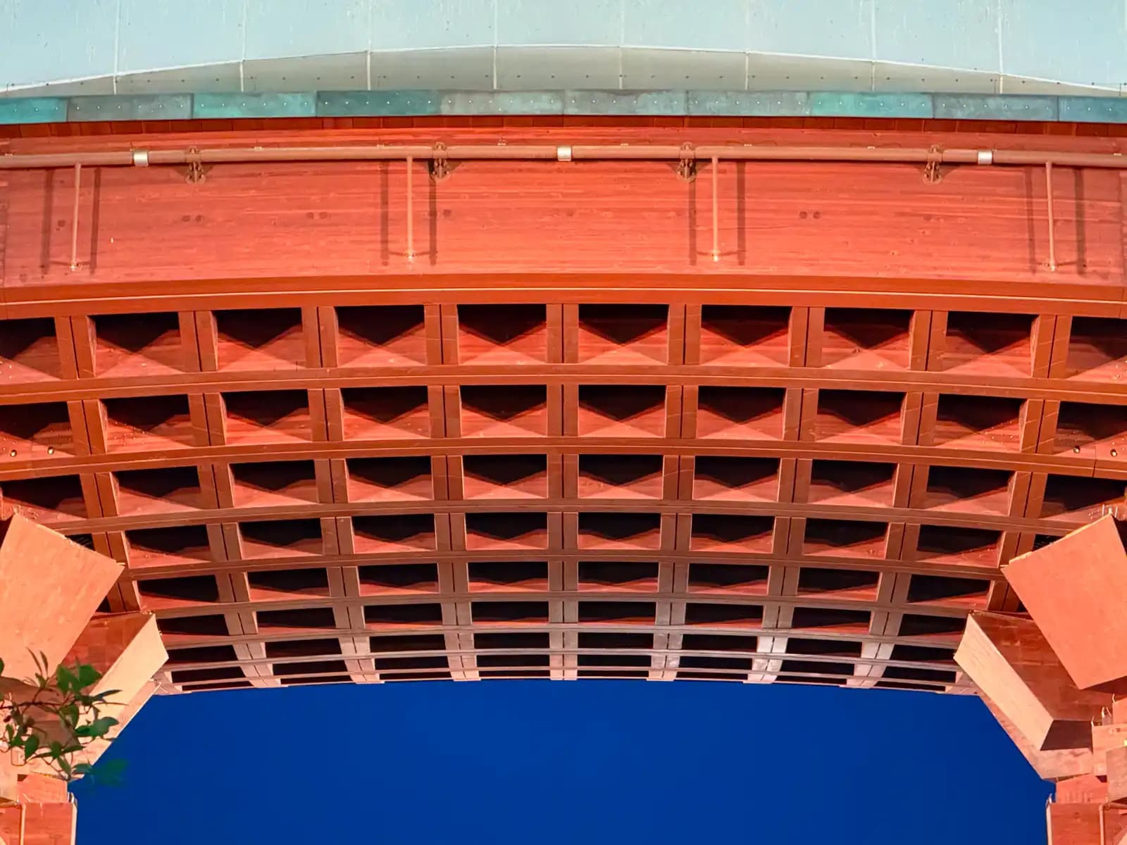 The underside of the Tsuzumi Gate's roof, lit in orange, with its grid of curved wooden beams against the evening sky.