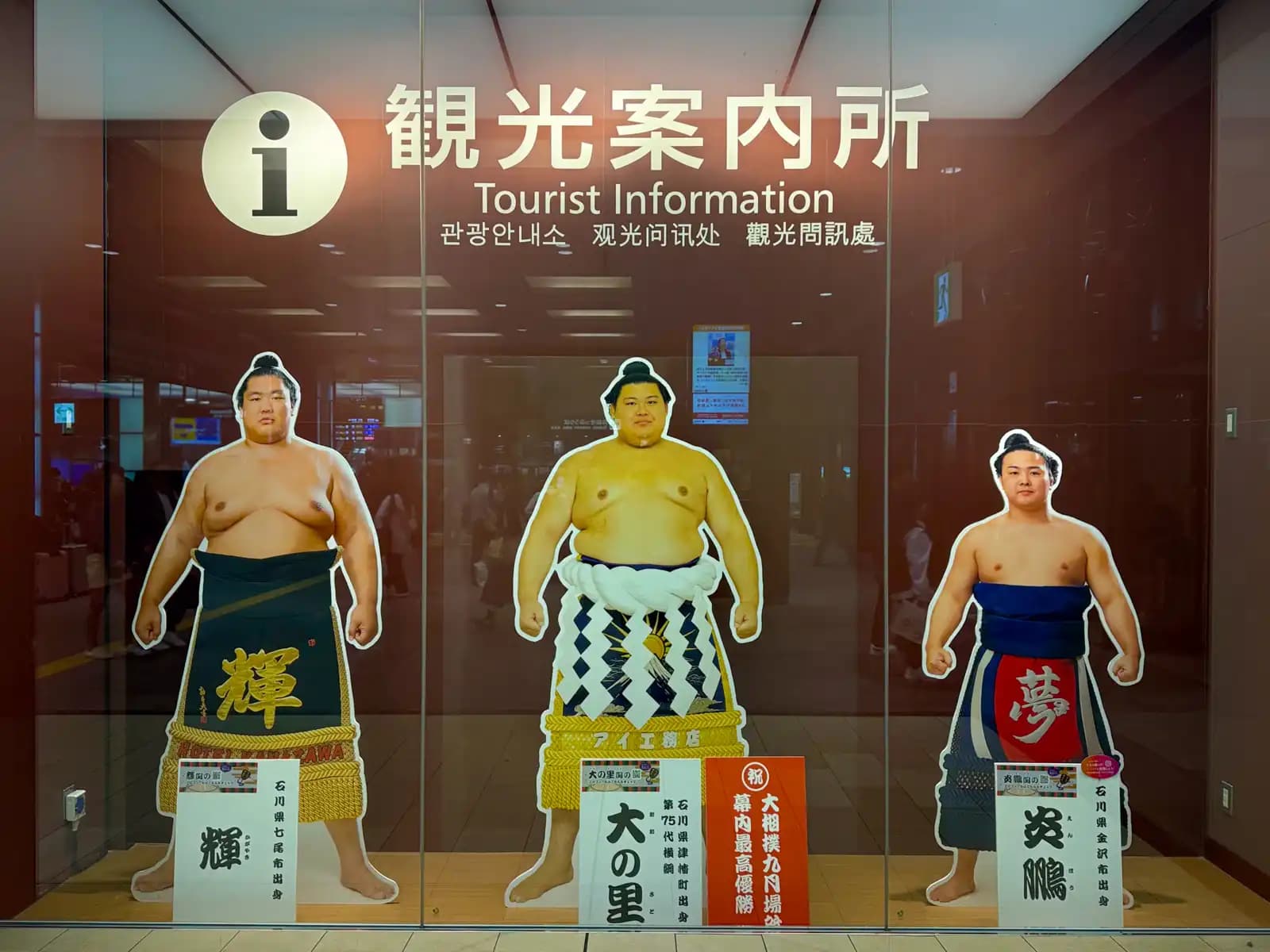 Life-size cutouts of three sumo wrestlers from Ishikawa Prefecture in the window of the station's tourist information center: Kagayaki from Nanao, the 75th yokozuna Onosato from Tsubata, and Enho from Kanazawa.