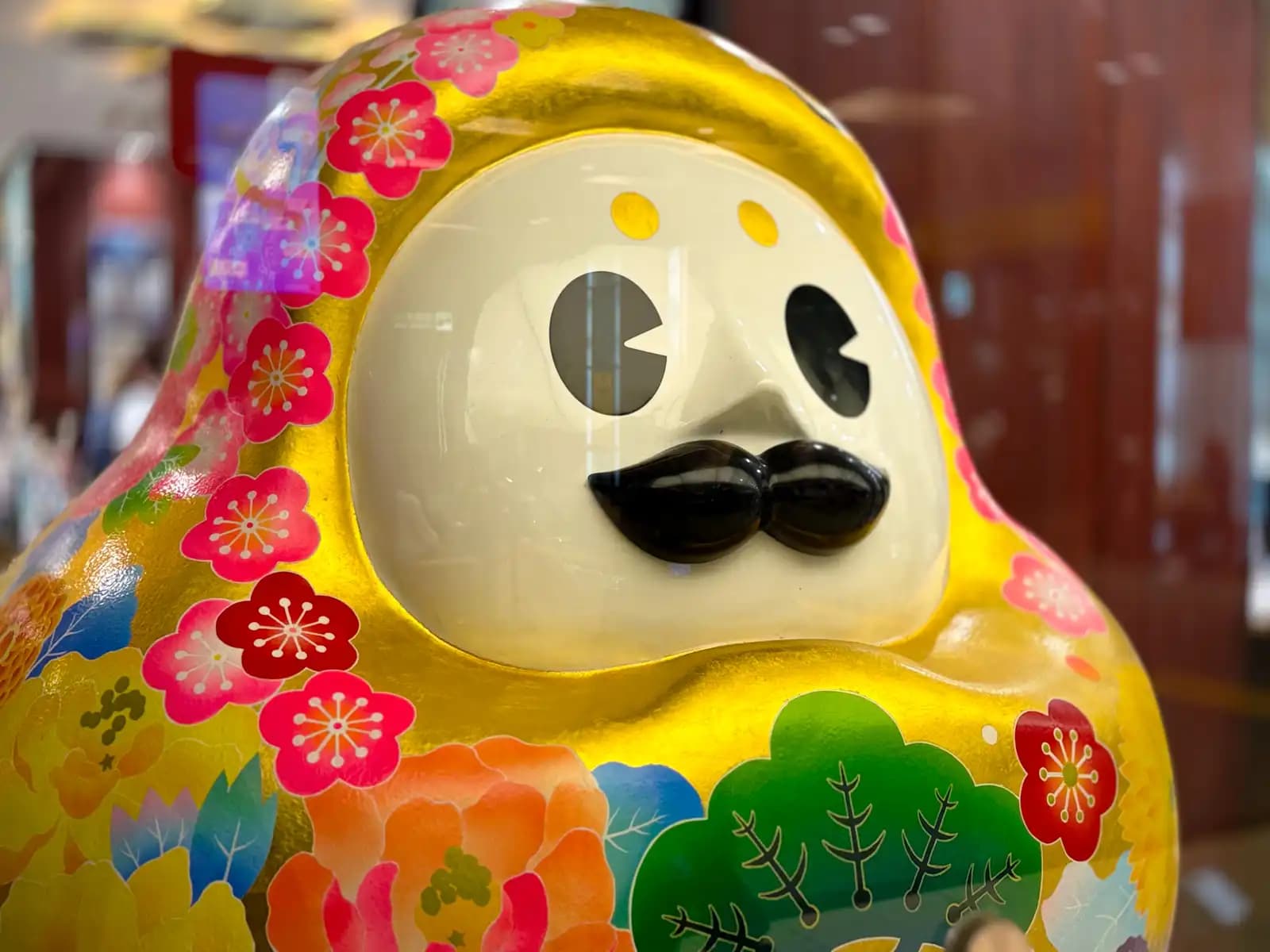 Hyakumansan, the tourism mascot of Ishikawa Prefecture, on display inside the station. It's based on a traditional local daruma-style doll and decorated with Ishikawa crafts: Kanazawa gold leaf on the body, Kaga Yuzen patterns, and a mustache made with Wajima lacquer techniques.