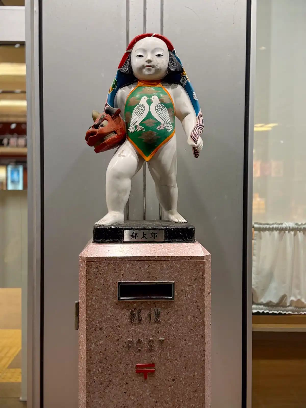 The Yutaro post box inside the station. It was installed in 1954 to mark the opening of the old Kanazawa Station building. The figure on top is a boy holding a red lion mask, made in the style of a Kaga doll, a traditional doll from the Kanazawa area. It's still a working post box.
