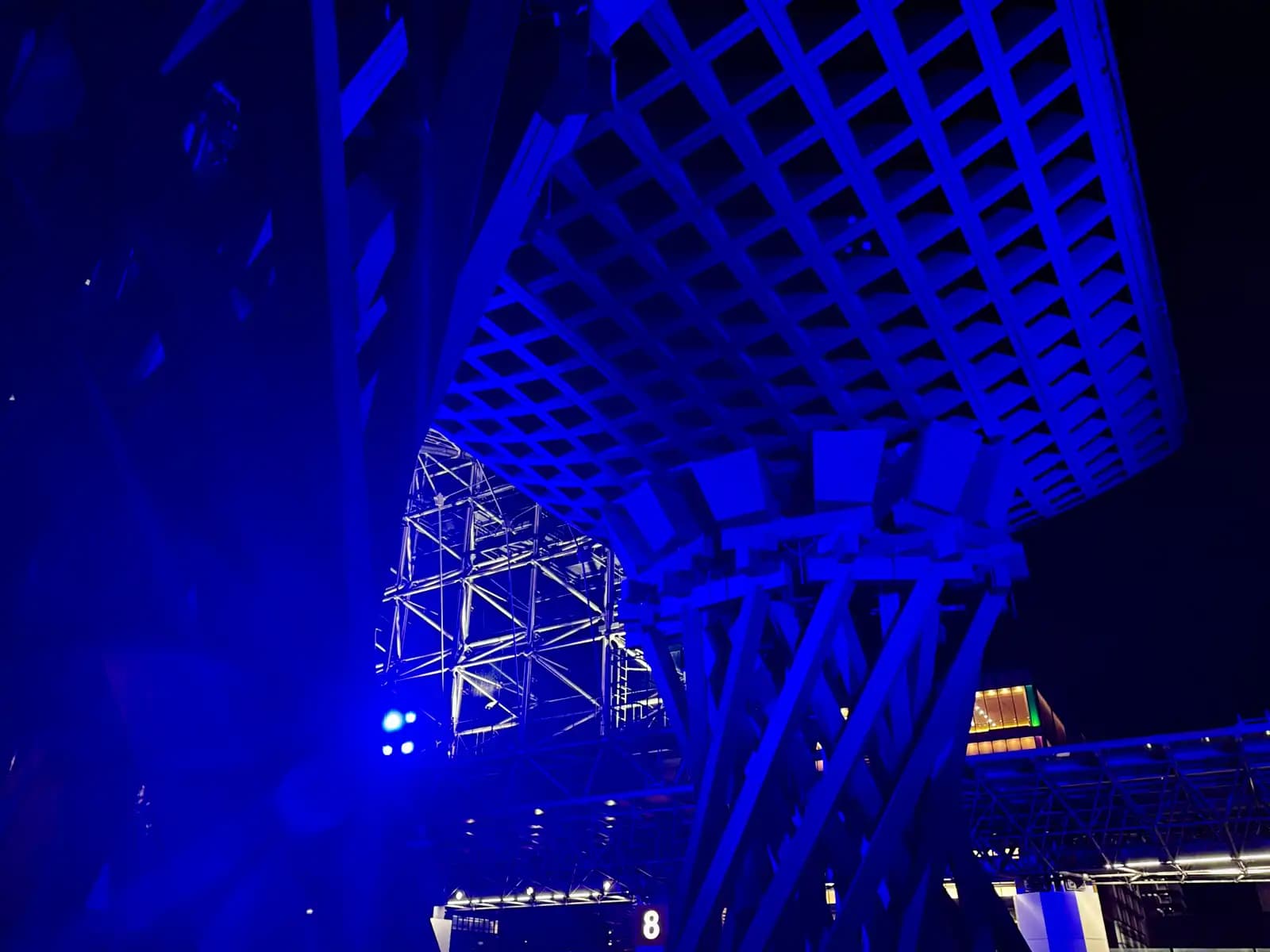 One pillar and part of the roof of the Tsuzumi Gate lit in blue at night, seen from below.