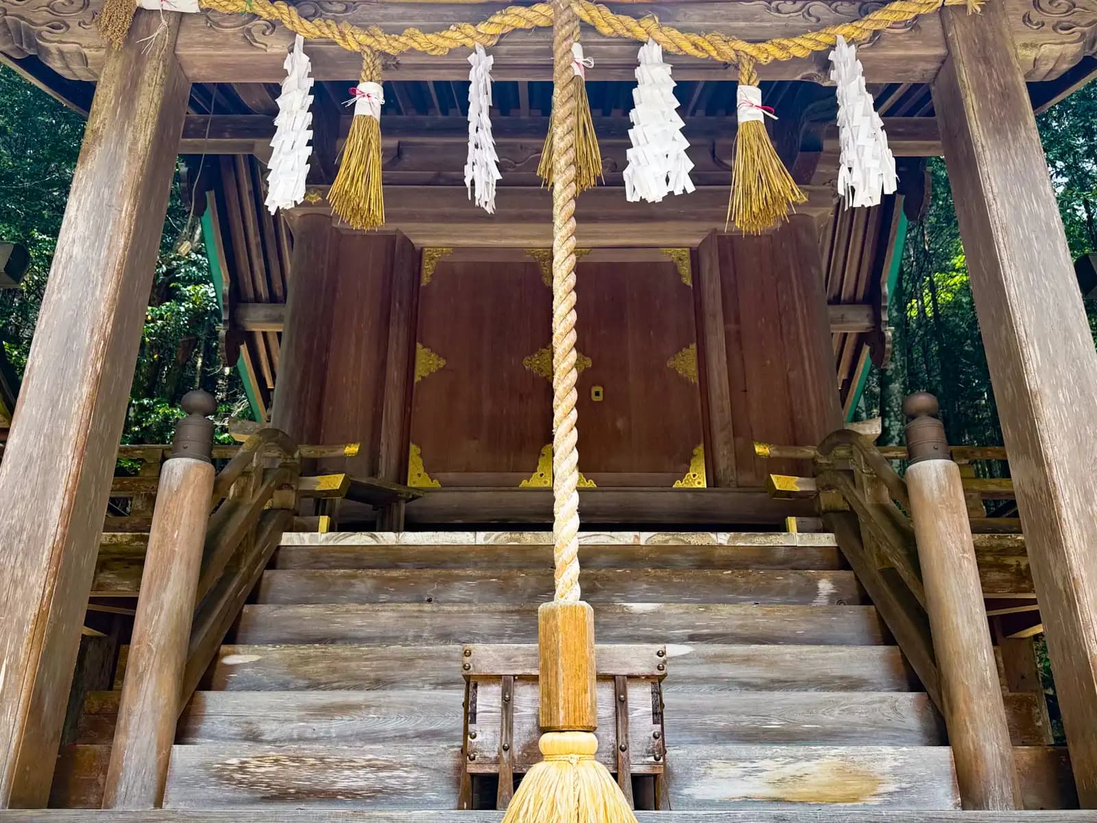 The front of the main hall: a thick braided bell-rope drops from a shimenawa strung with shide and straw tassels, above the closed doors with their gilded fittings.