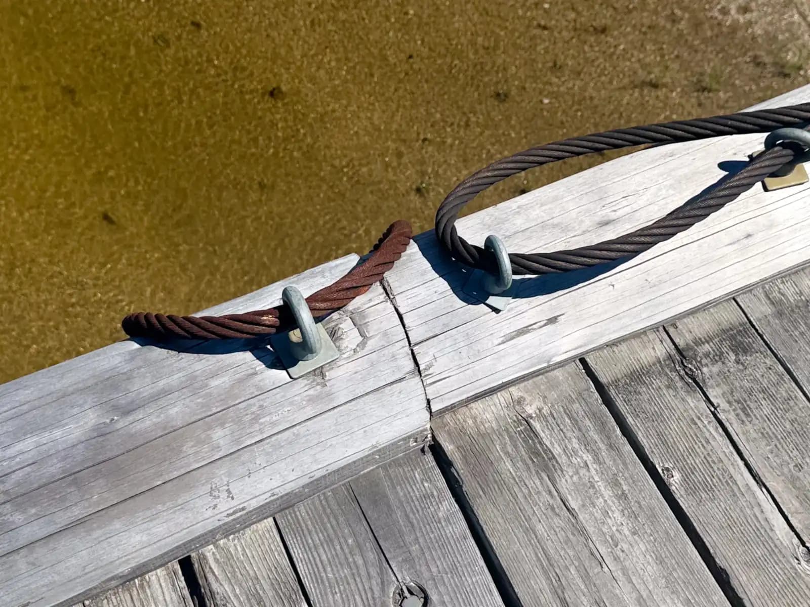 Detail of the tethering system: each section of deck is tied to the piers by thick wire rope threaded through steel eyes. In a flood the deck lifts and swings downstream on these lines instead of being lost.