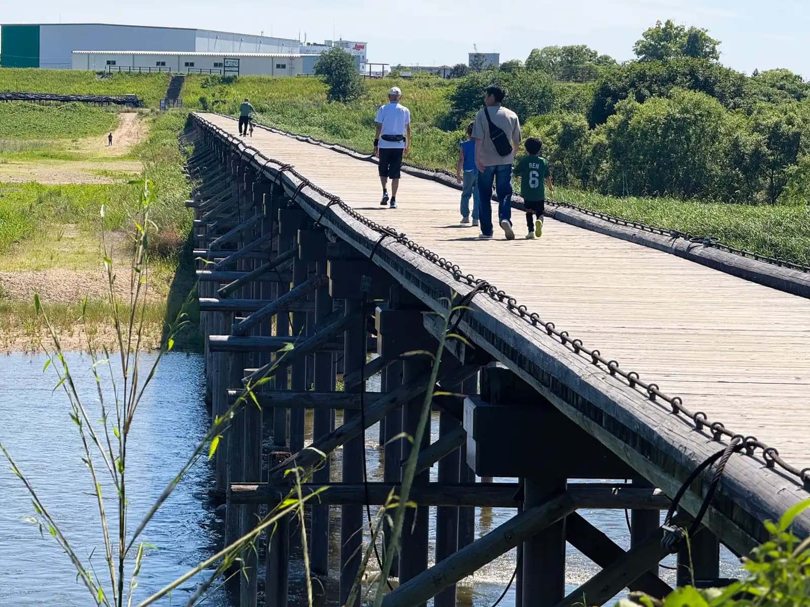 A family strolls across Nagare-bashi, the railless wooden footbridge over the Kizu River in Yawata, Kyoto. The looped steel cables running along the deck edge are what keep the planks from washing away for good when the river floods.