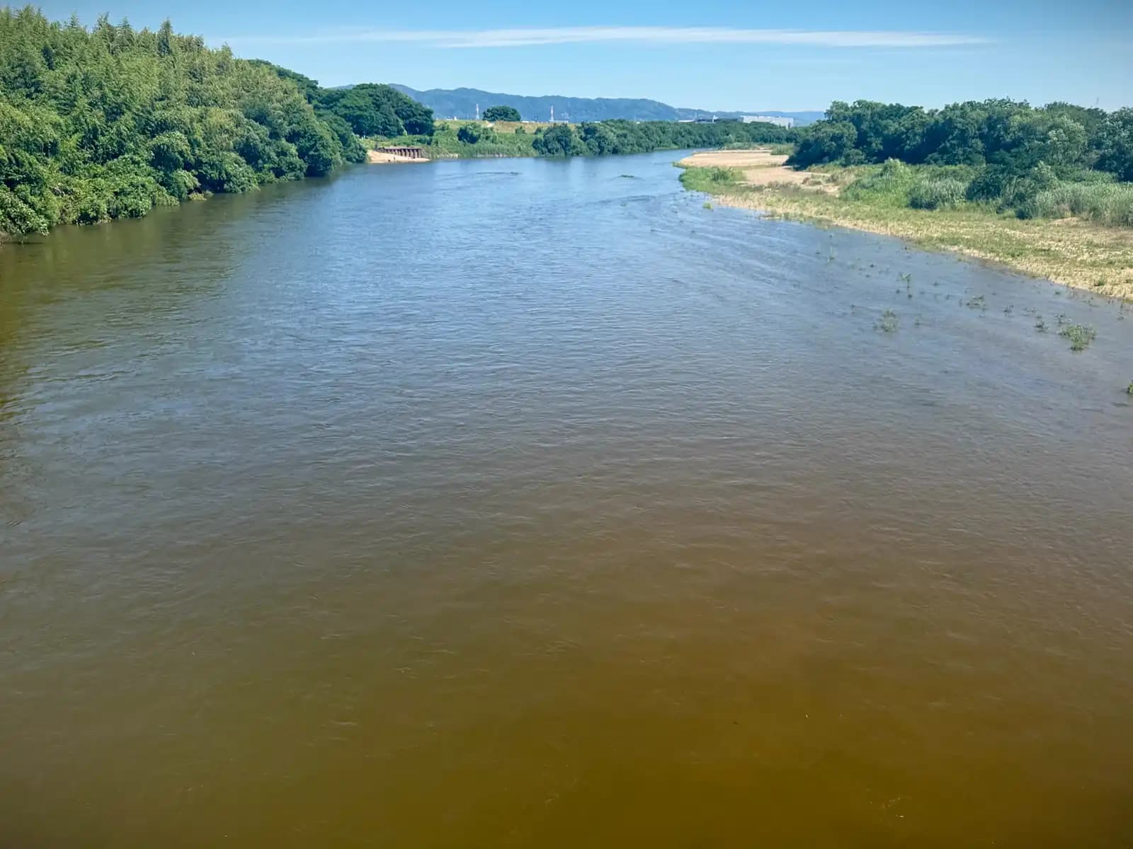 The Kizu River seen from the bridge, its wide channel running brown between green banks. The far hills mark the edge of the Kyoto basin.