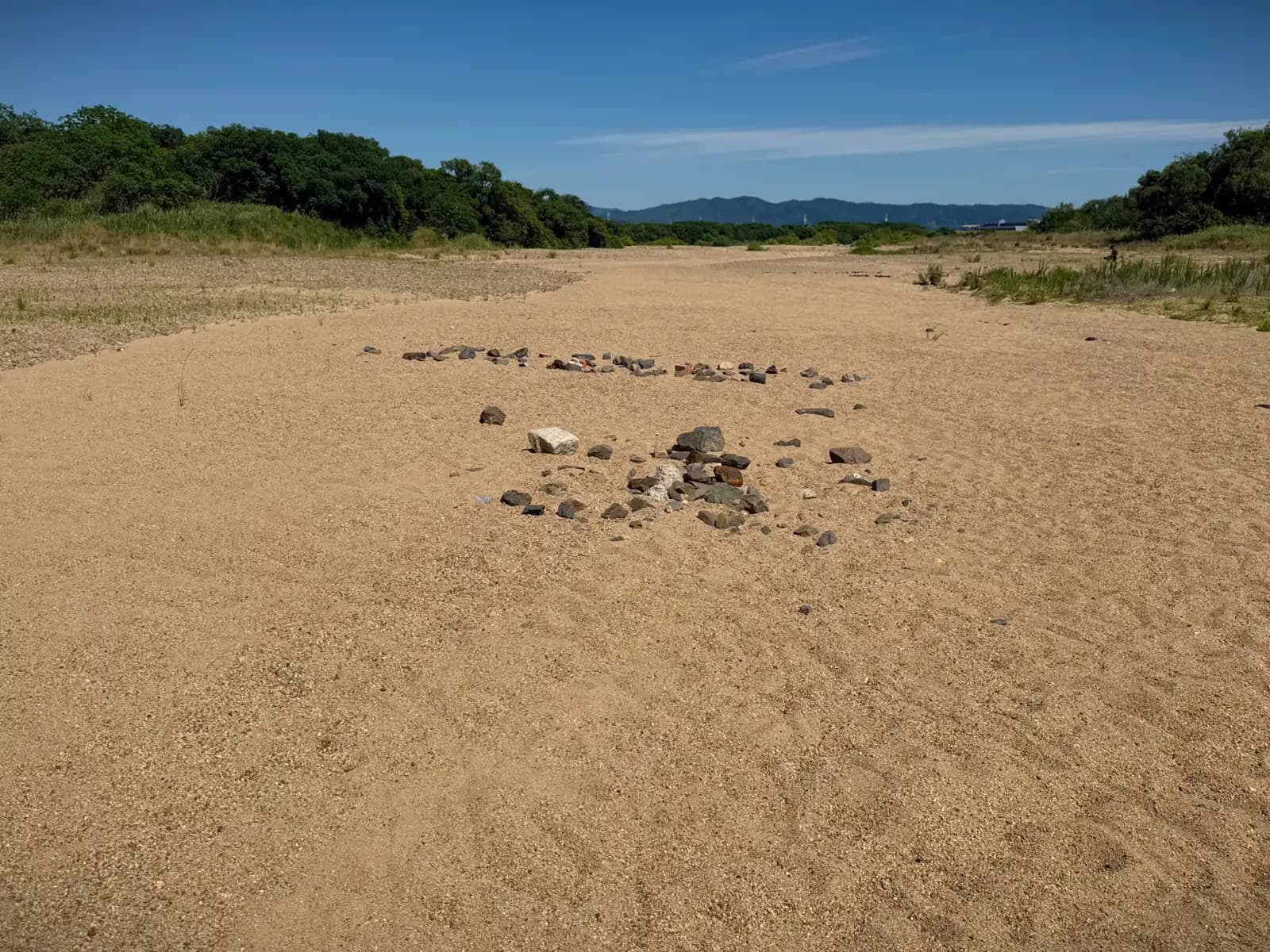 On the dry bed of the Kizu, someone has laid dark stones into a word. Visitors sometimes spell out messages here to be read from the bridge above. Distant hills close off the far bank.