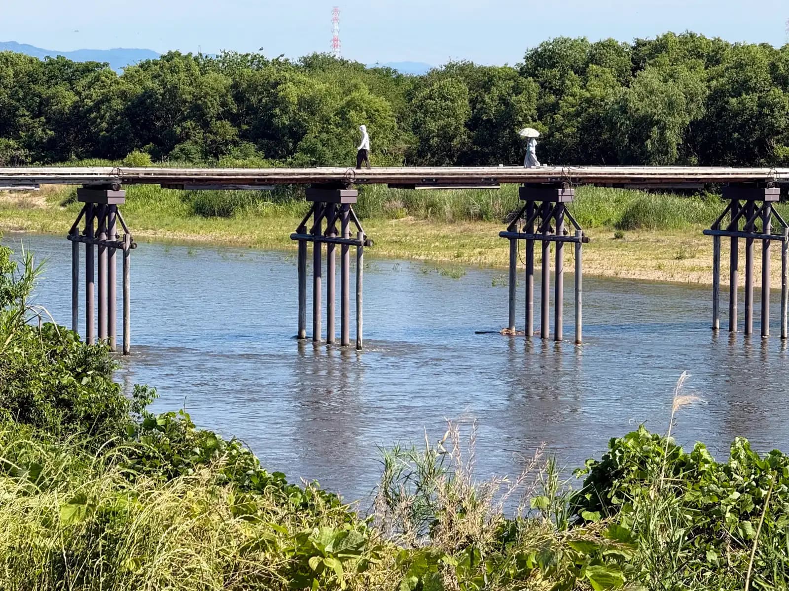 Two figures with parasols pass midway across, the river running full beneath the long line of piers.