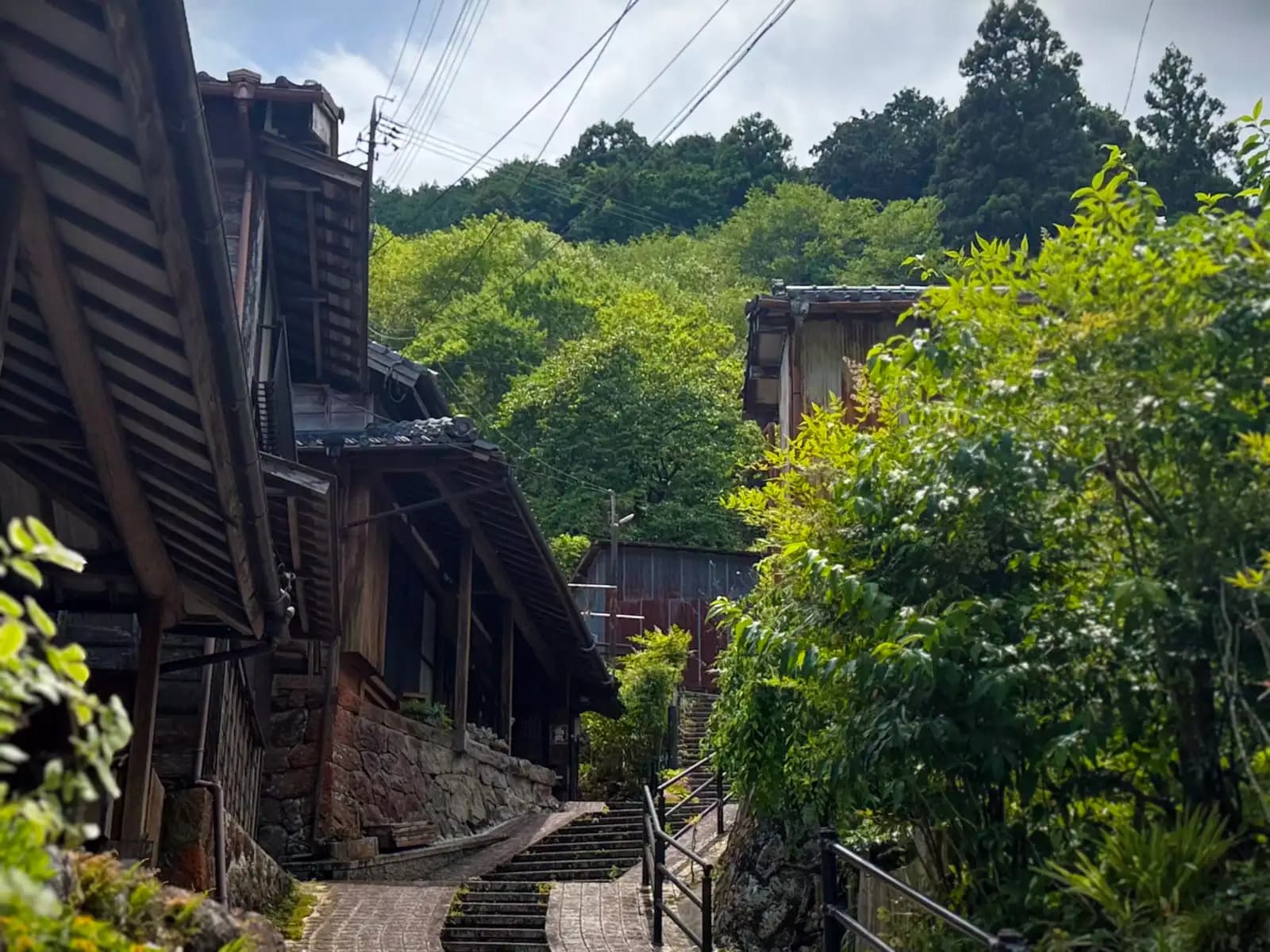 The path climbs between old wooden houses and the forested hillside.