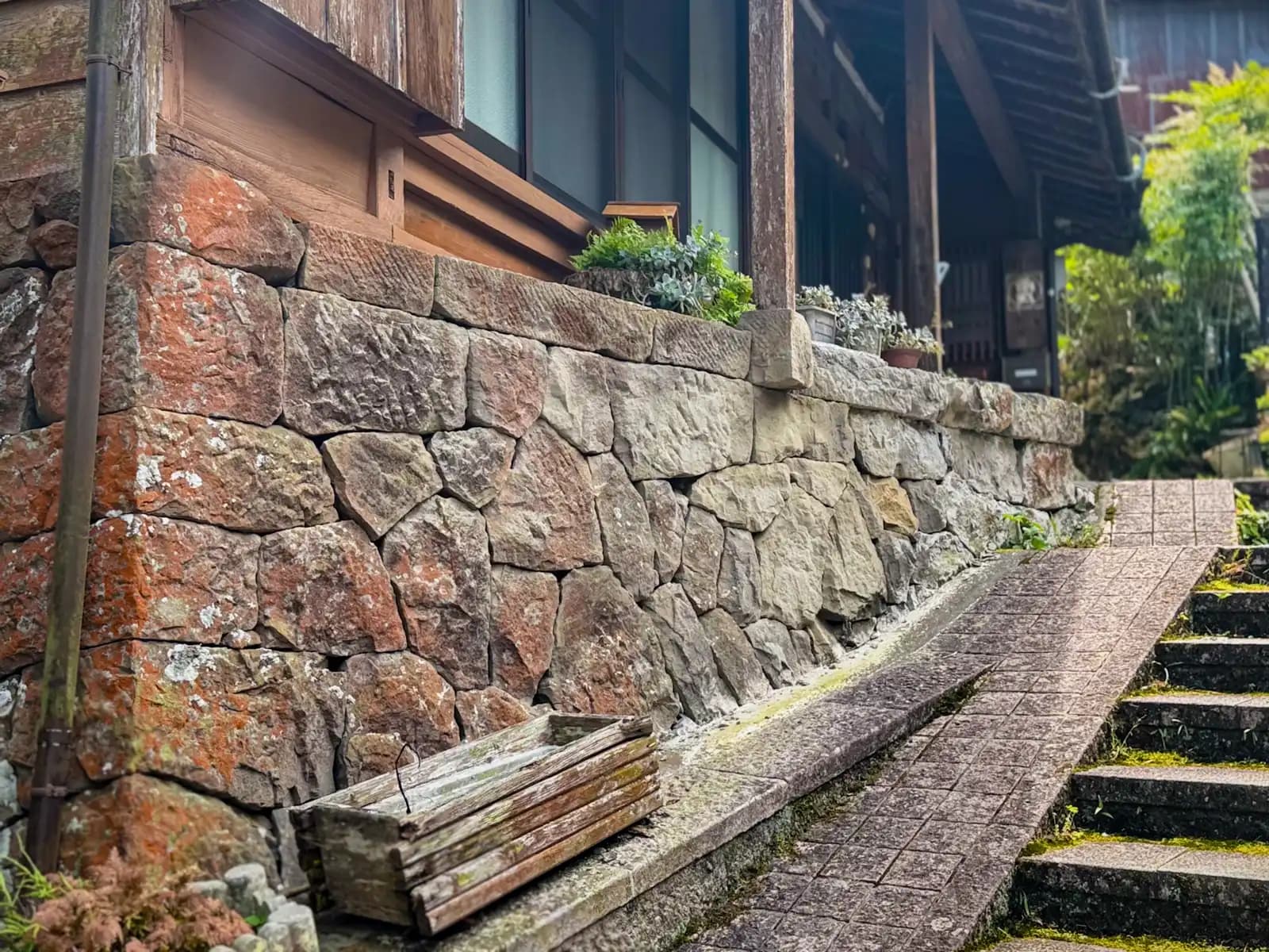 A stone retaining wall holding up the base of a wooden house, with a ramp and steps alongside.