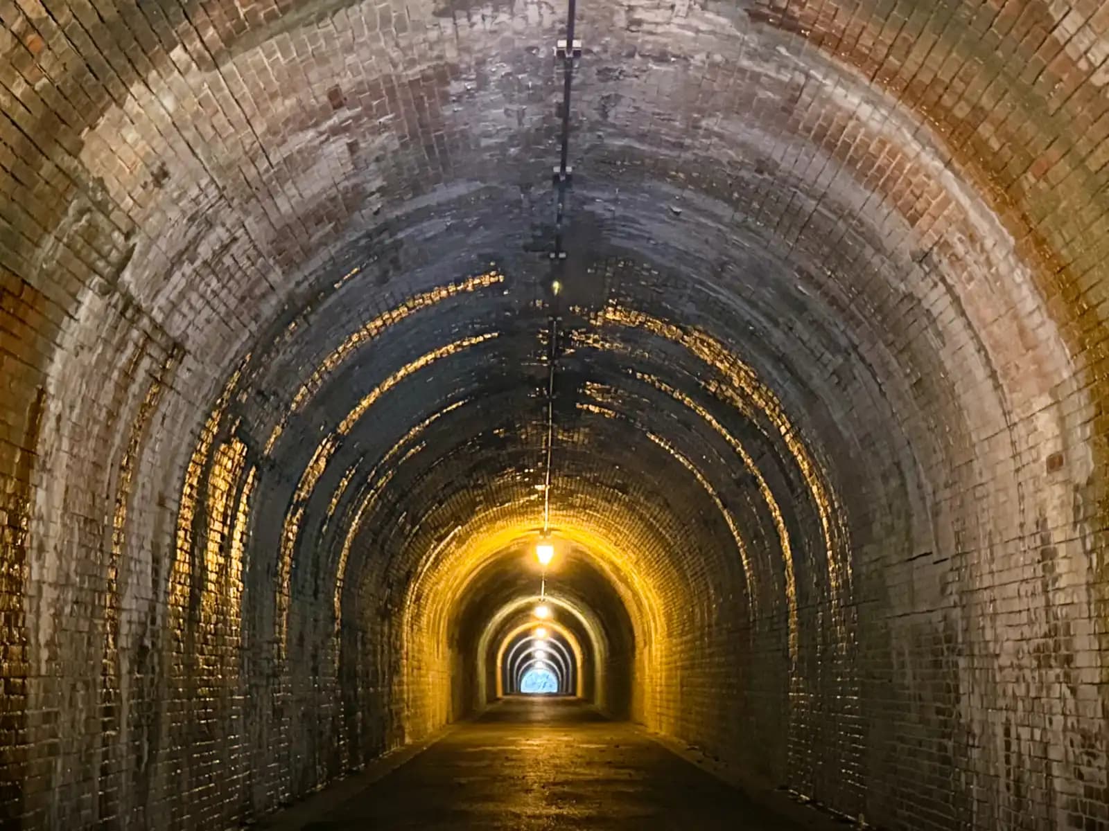 Inside the tunnel, looking down the long brick vault toward the lamps and the exit.