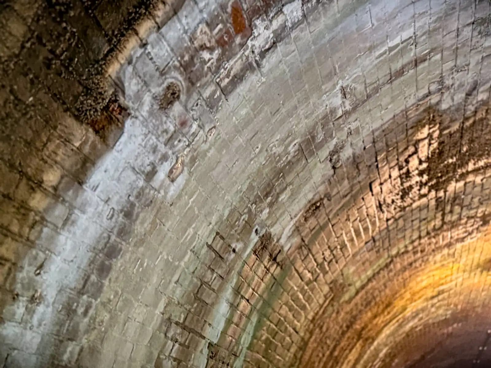 Close up of the curved brick ceiling inside, pale with age and lit by a lamp.