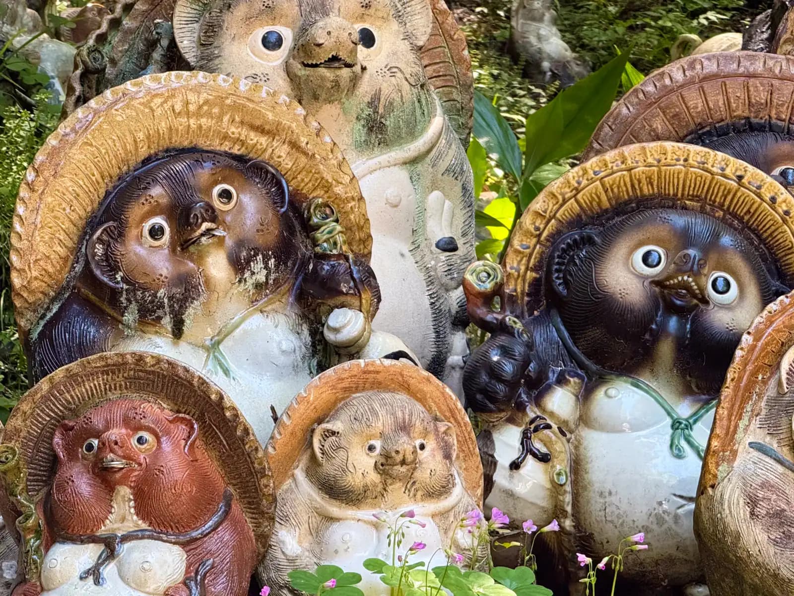 A huddle of tanuki, each in its woven straw hat, crowding together in the undergrowth.