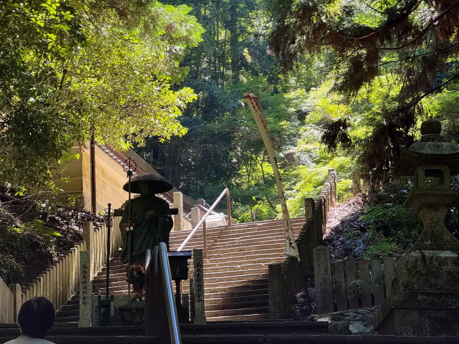 The climb continues past a straw-hatted pilgrim statue of Kōbō Daishi as the stone steps rise into the cedars.