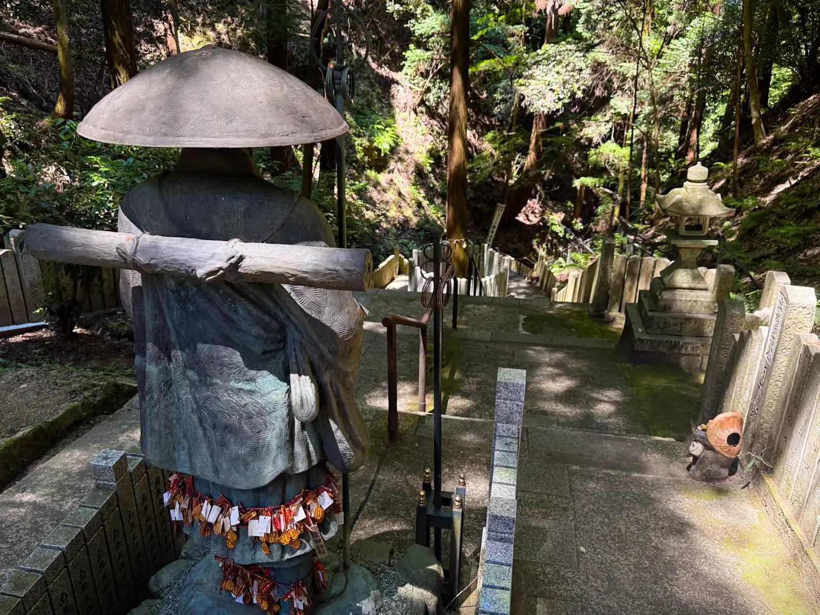 Looking back down the mountain from behind the pilgrim statue, its shoulders draped with folded paper fortunes.