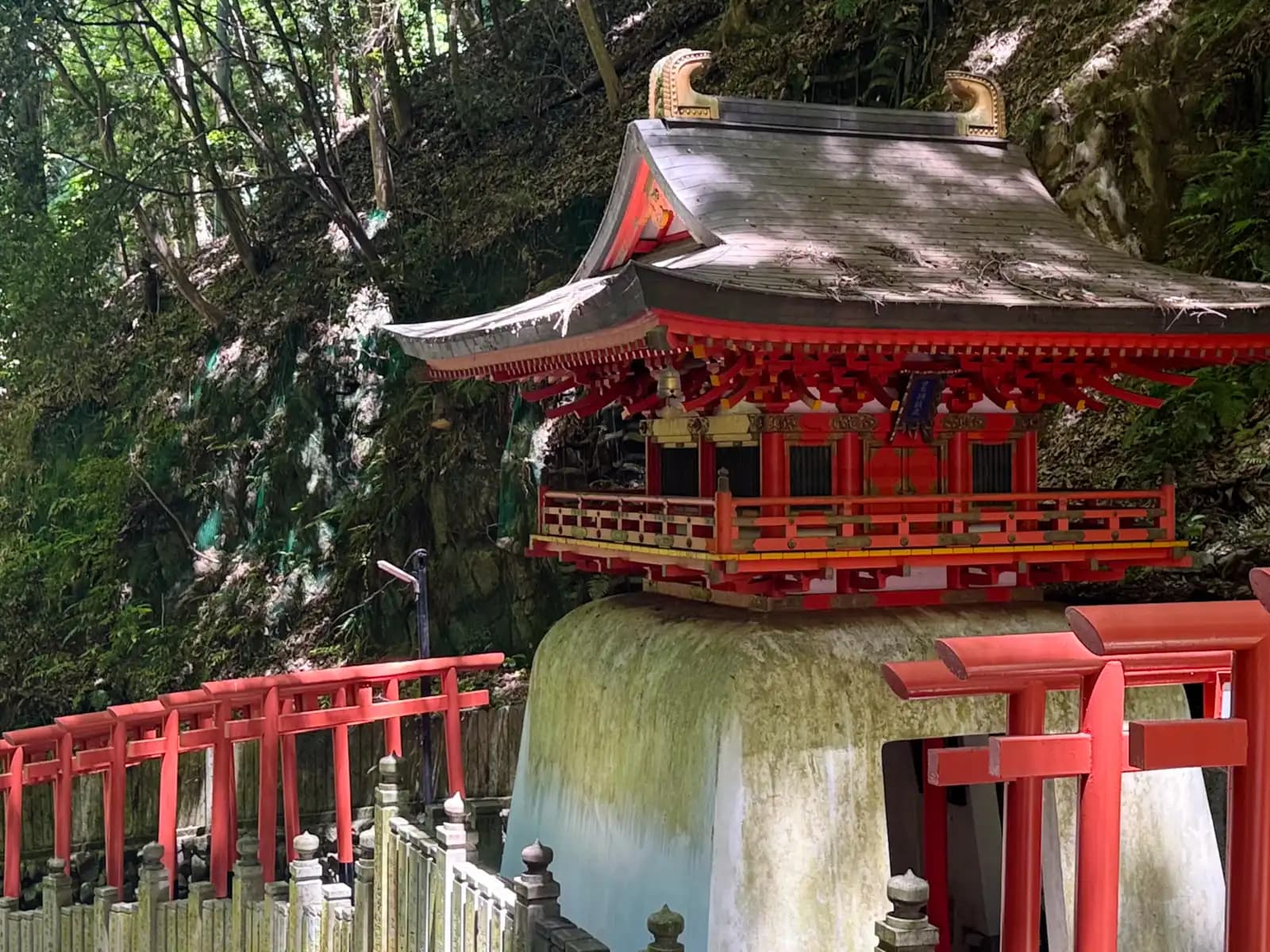 An ornate vermilion shrine perched on its rock outcrop, lines of torii running to it on both sides.