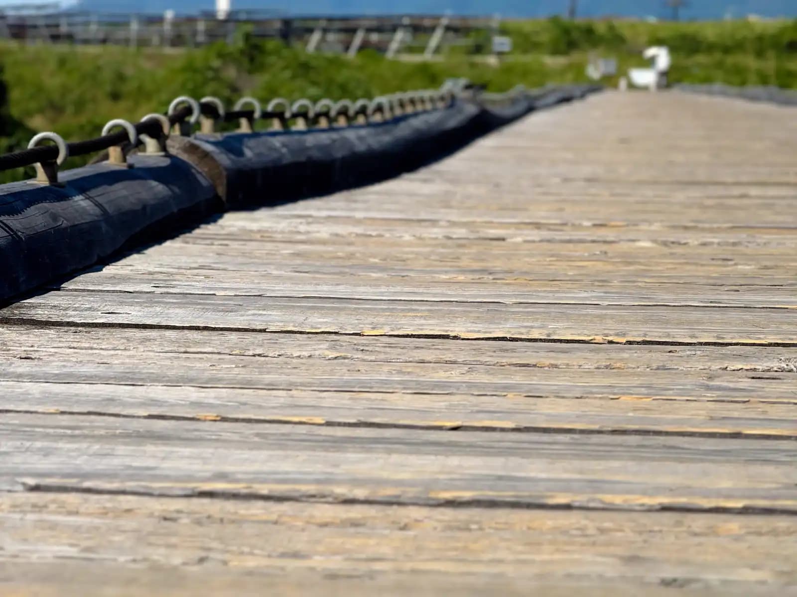 Deck level: the black rubber-sheathed guide cable and its ring bolts run along the planks, the only thing resembling an edge on the whole bridge.