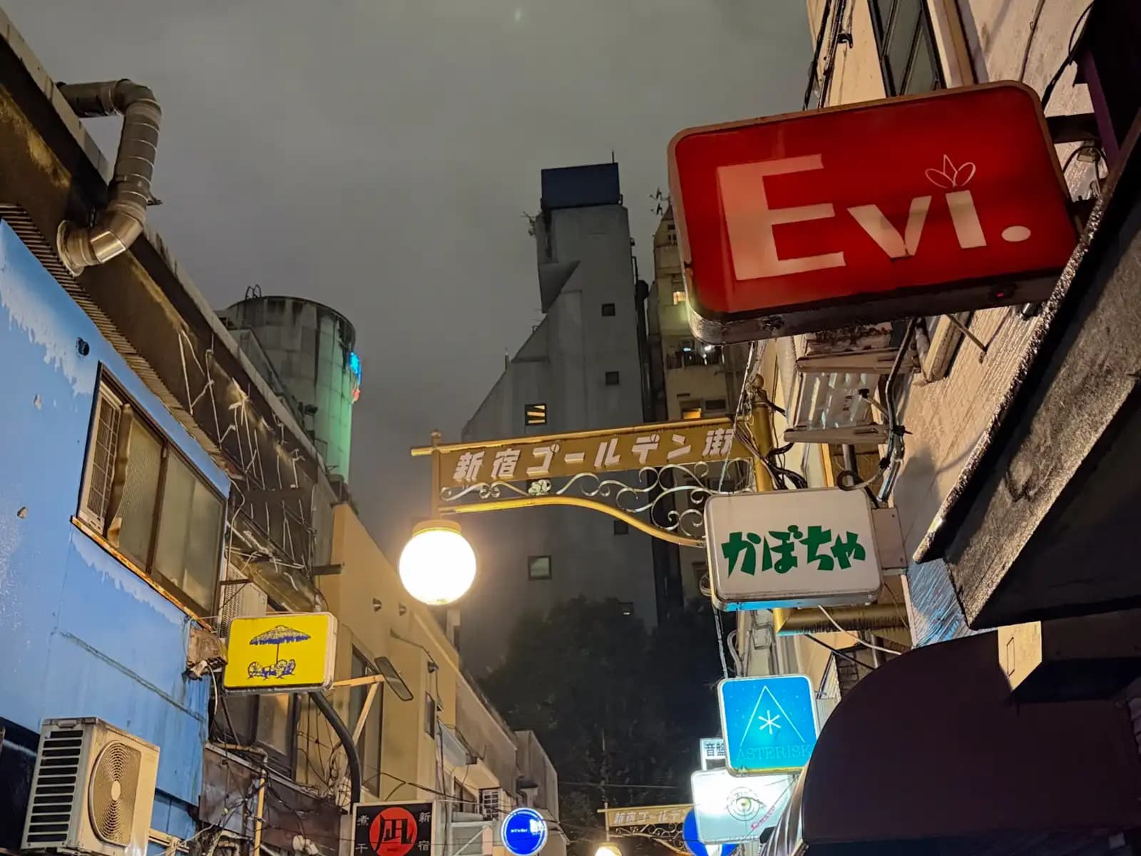 The Shinjuku Golden Gai arch with a round lamp, next to signs for Evi., Kabocha and Asterisk.