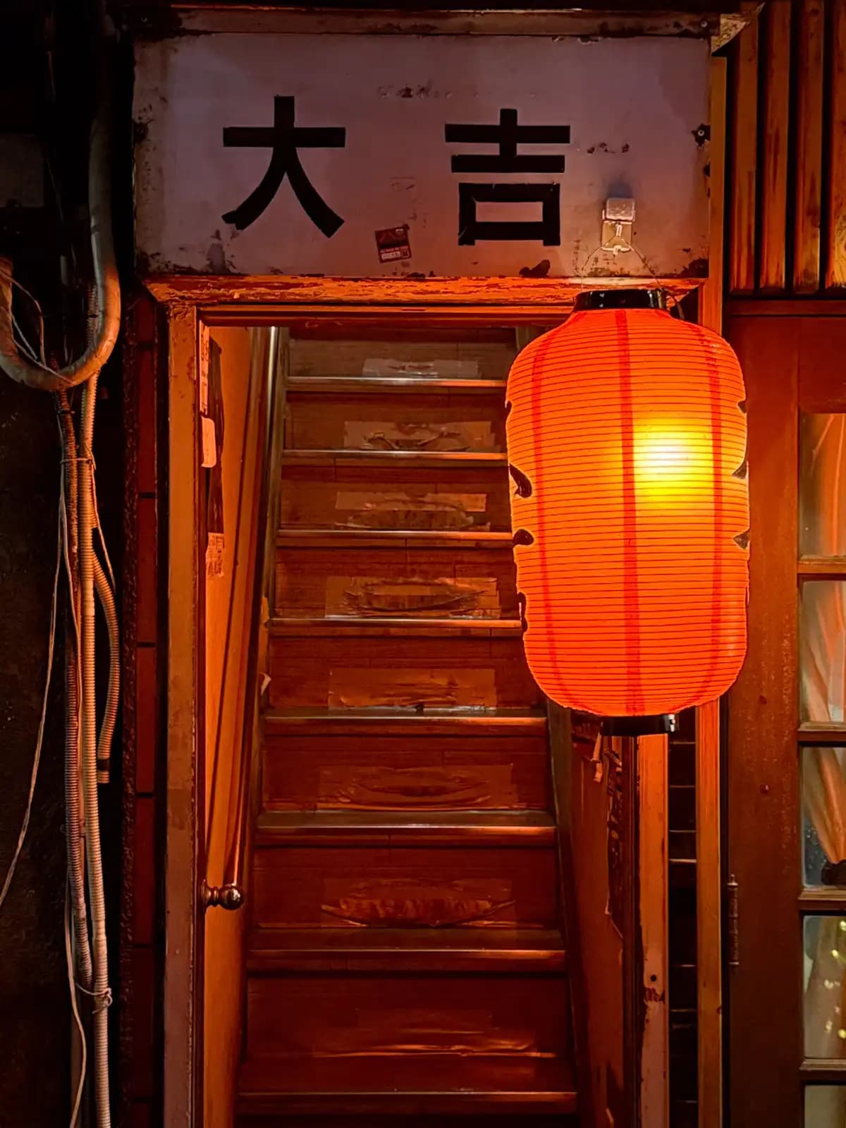 A red paper lantern glows next to a wooden staircase under an old sign that reads Daikichi.