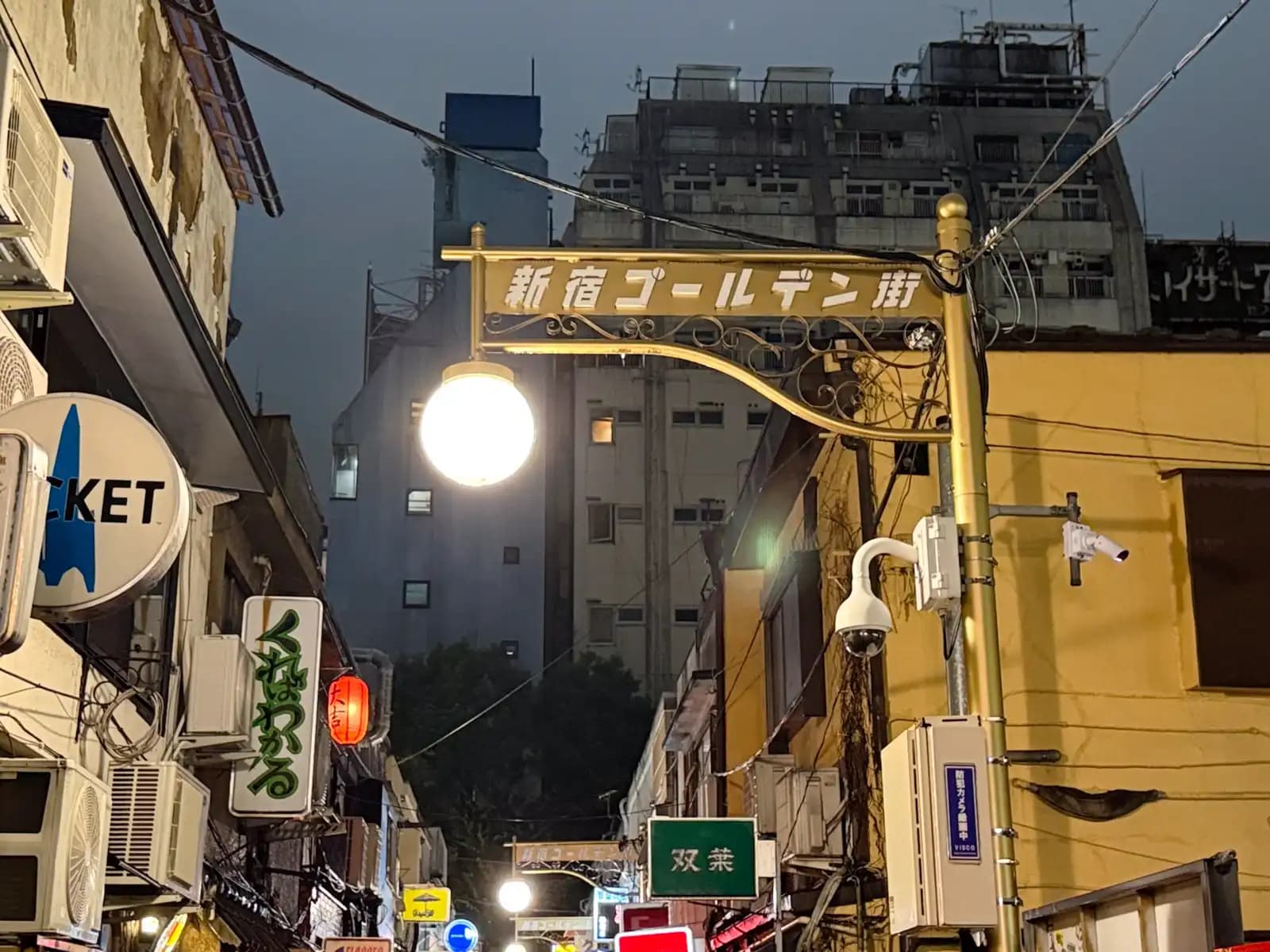 The Golden Gai street sign and lamp against a cloudy night sky, with signs for Rocket, Kureba Wakaru and Futaba below.