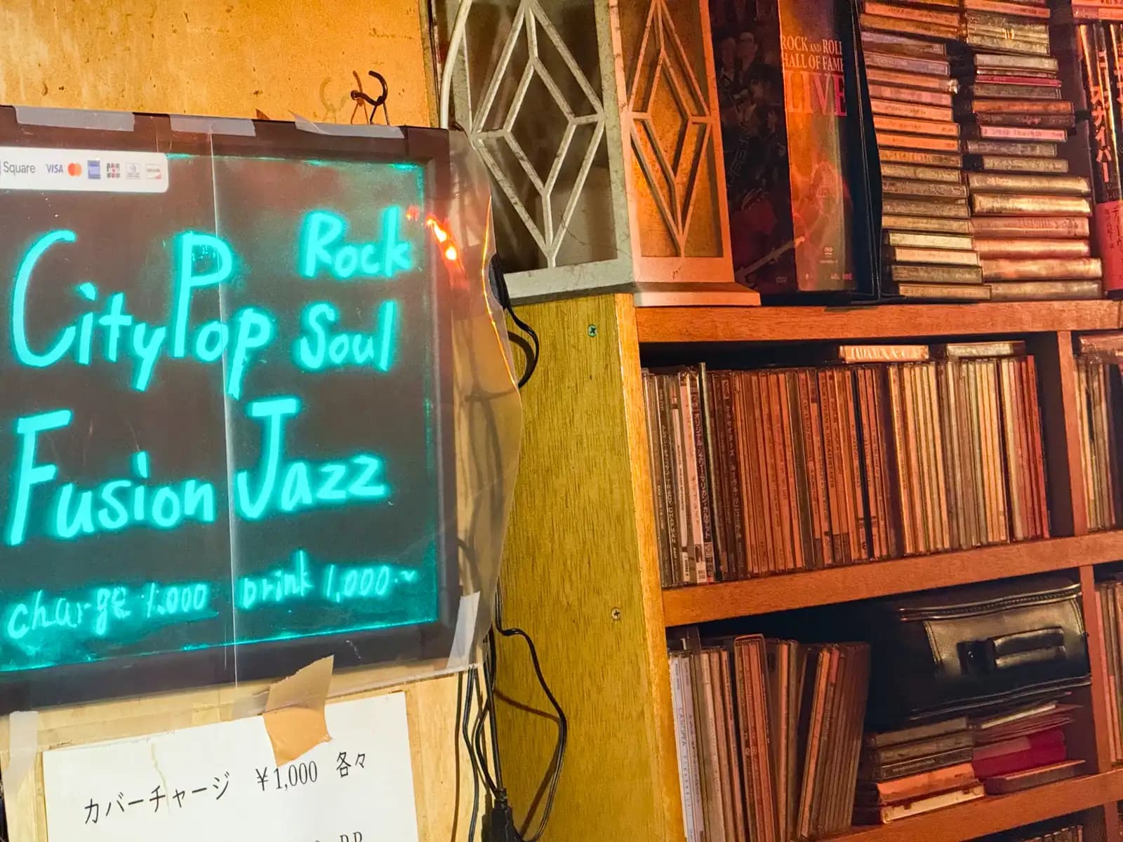 A glowing board lists City Pop, Rock, Soul, Fusion and Jazz, with a ¥1,000 cover charge, next to shelves packed with CDs.