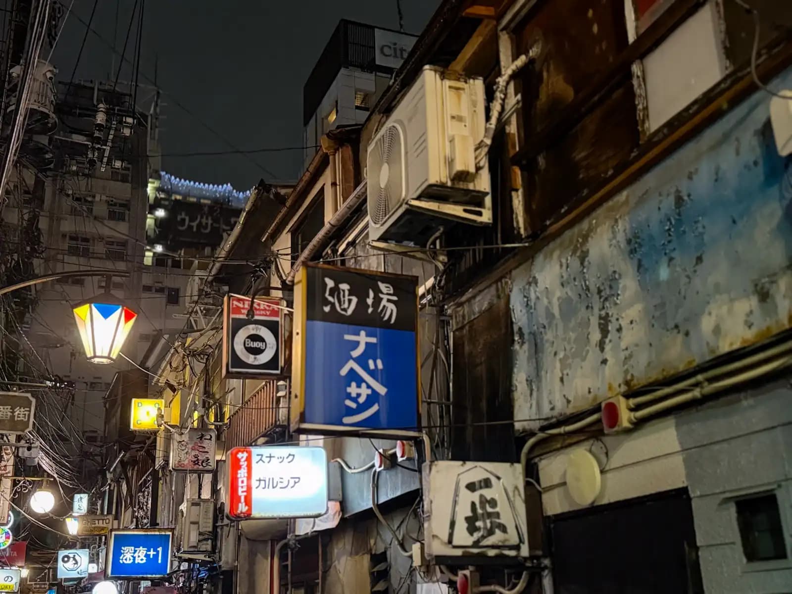Looking up at old bar signs: the blue Nabesan sign, Snack Garcia and Buoy, with peeling paint on the wall beside them.