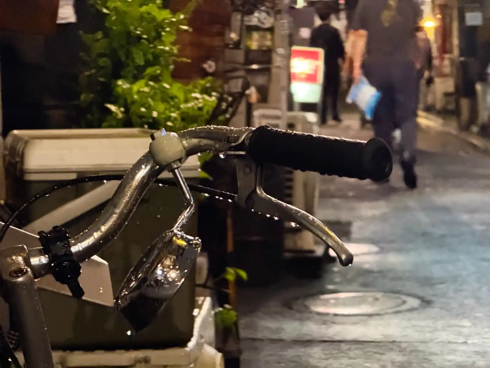 Raindrops on a bicycle handlebar and bell, with people walking by.