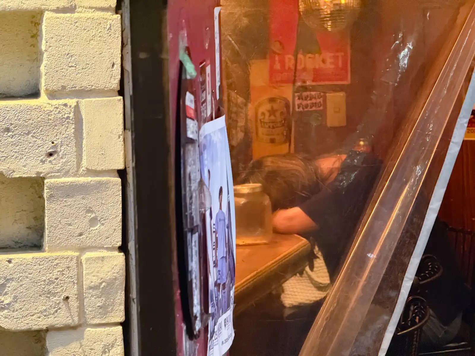 Through a plastic curtain, someone has their head down on the bar counter next to a glass jar.