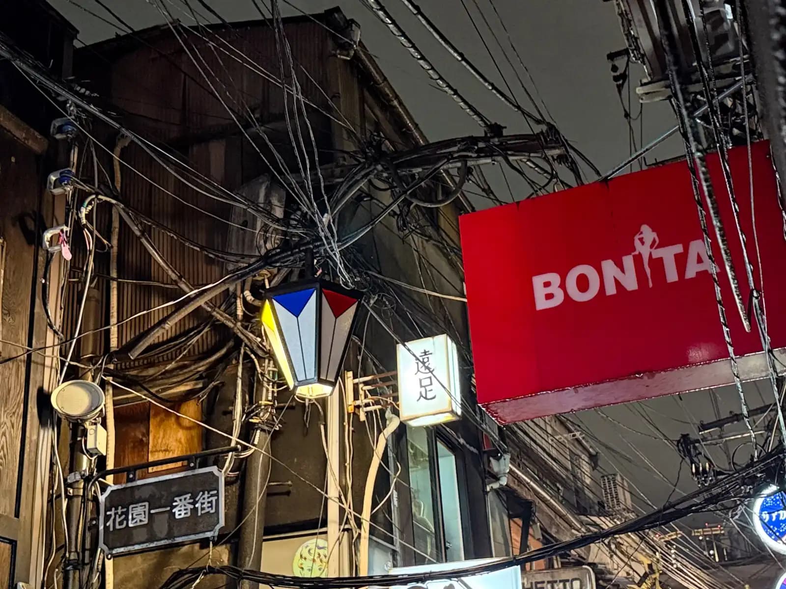 Wires going every which way around a street lamp, with the Hanazono Ichibangai street sign and a big red Bonita sign.