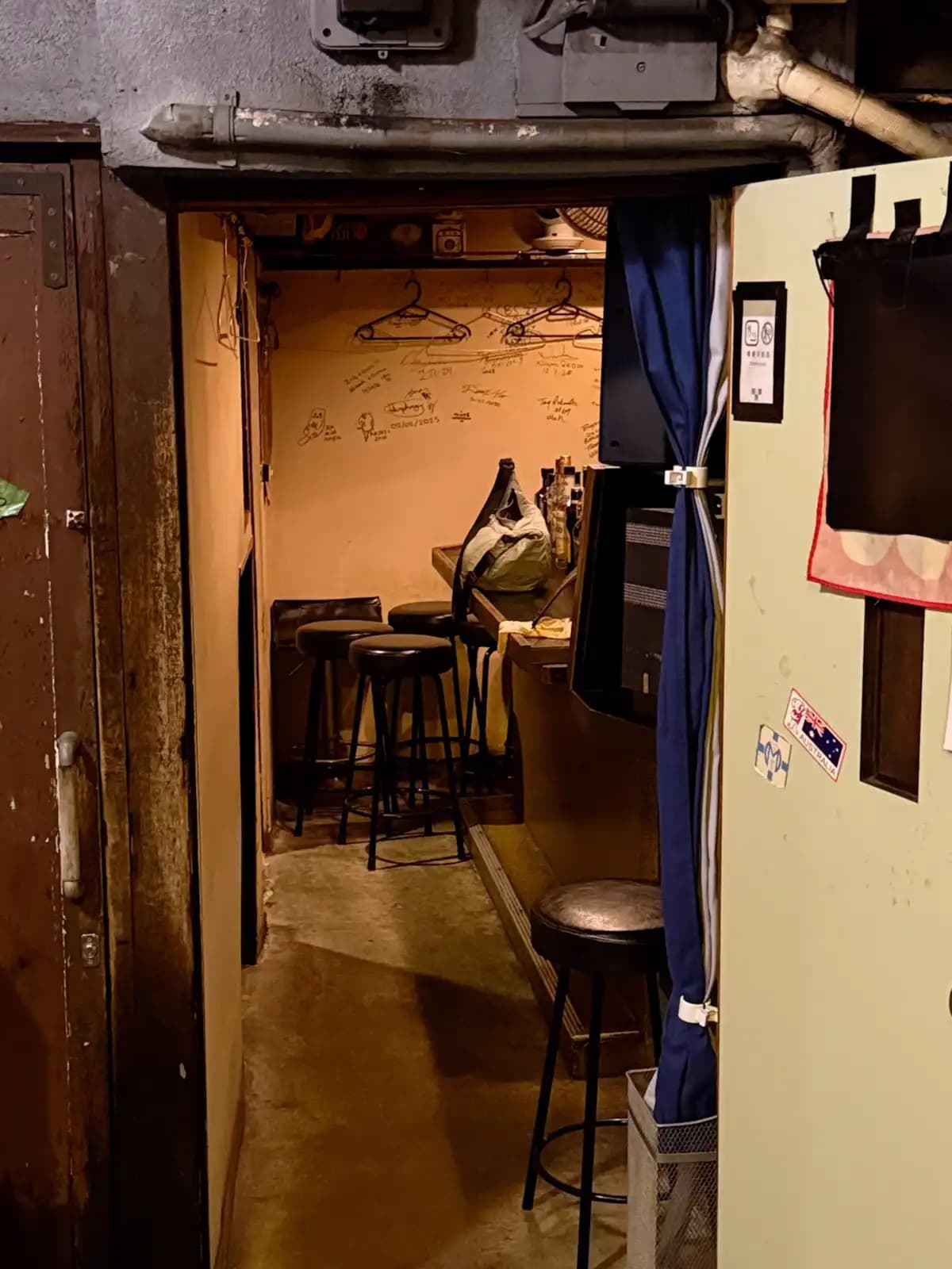 A peek into a tiny empty bar: a few stools at the counter, hangers on the wall and signatures scribbled all over it.