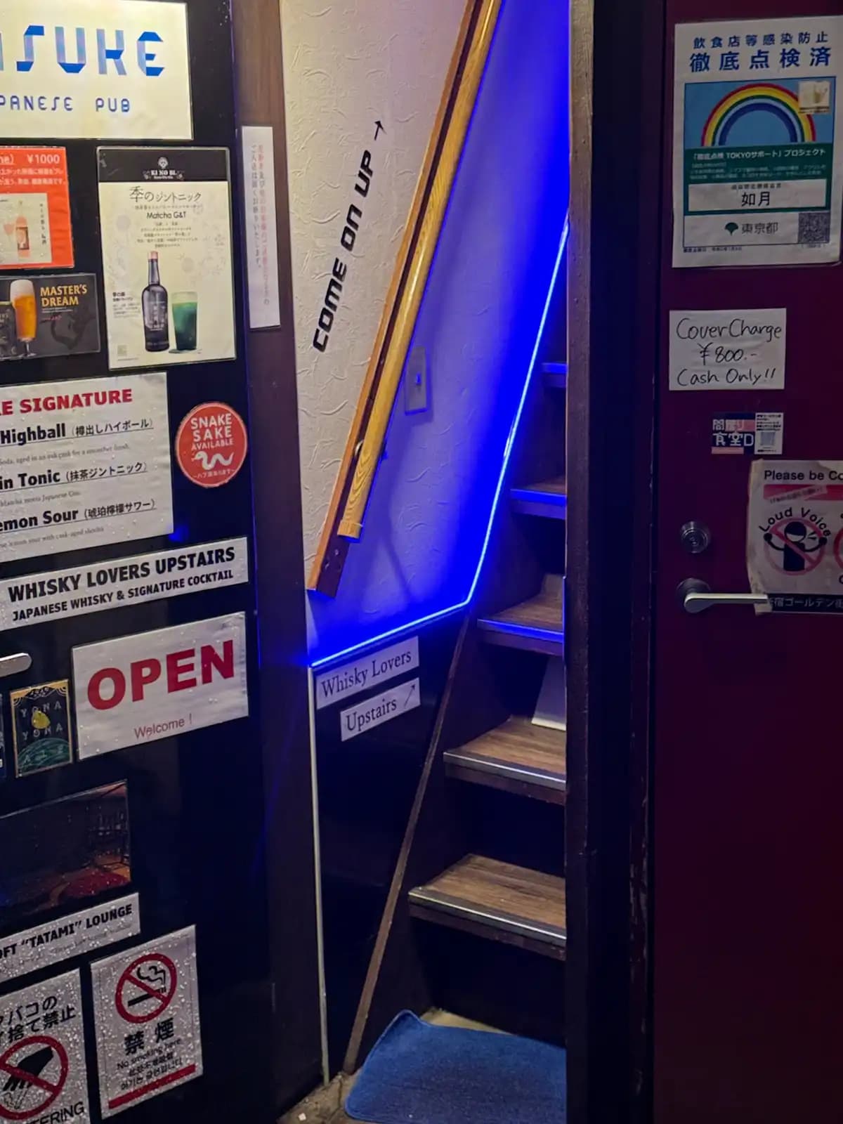 A steep, narrow staircase lit in blue with "Come on up" and "Whisky Lovers Upstairs" signs, and an 800 yen, cash-only cover charge on the door.