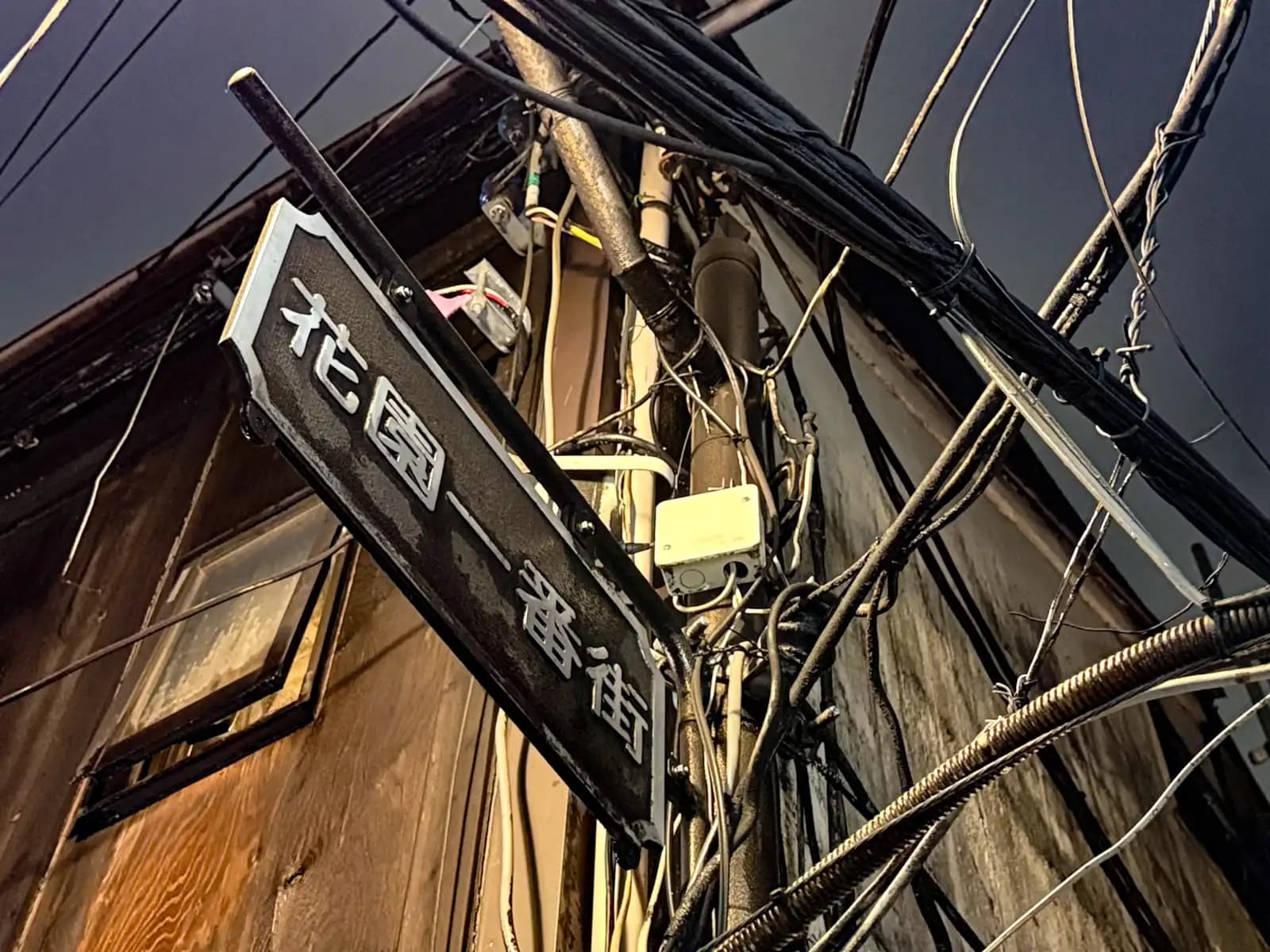 The Hanazono Ichibangai street sign on a pole, surrounded by a mess of wires and cables.