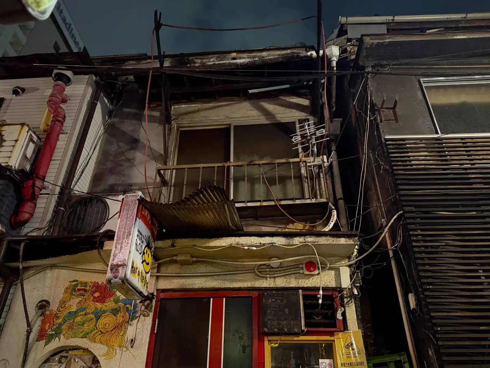 Looking up at the old building above Hair of the Dogs: a rusty balcony, a TV antenna, a red pipe, and a painted lion by the door.
