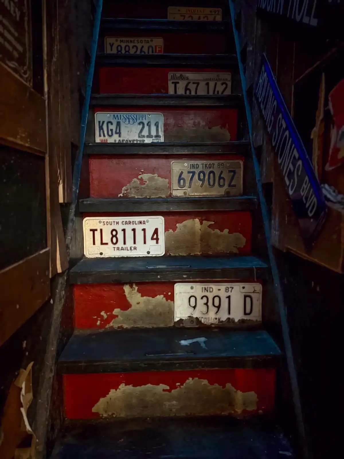 Old US license plates from Mississippi, South Carolina, Indiana and other states nailed to the steps of a steep red staircase.