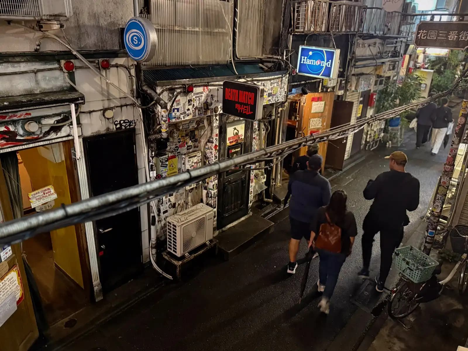 Looking down from above at people walking along a wet lane past the Death Match in Hell and Hamond signs.