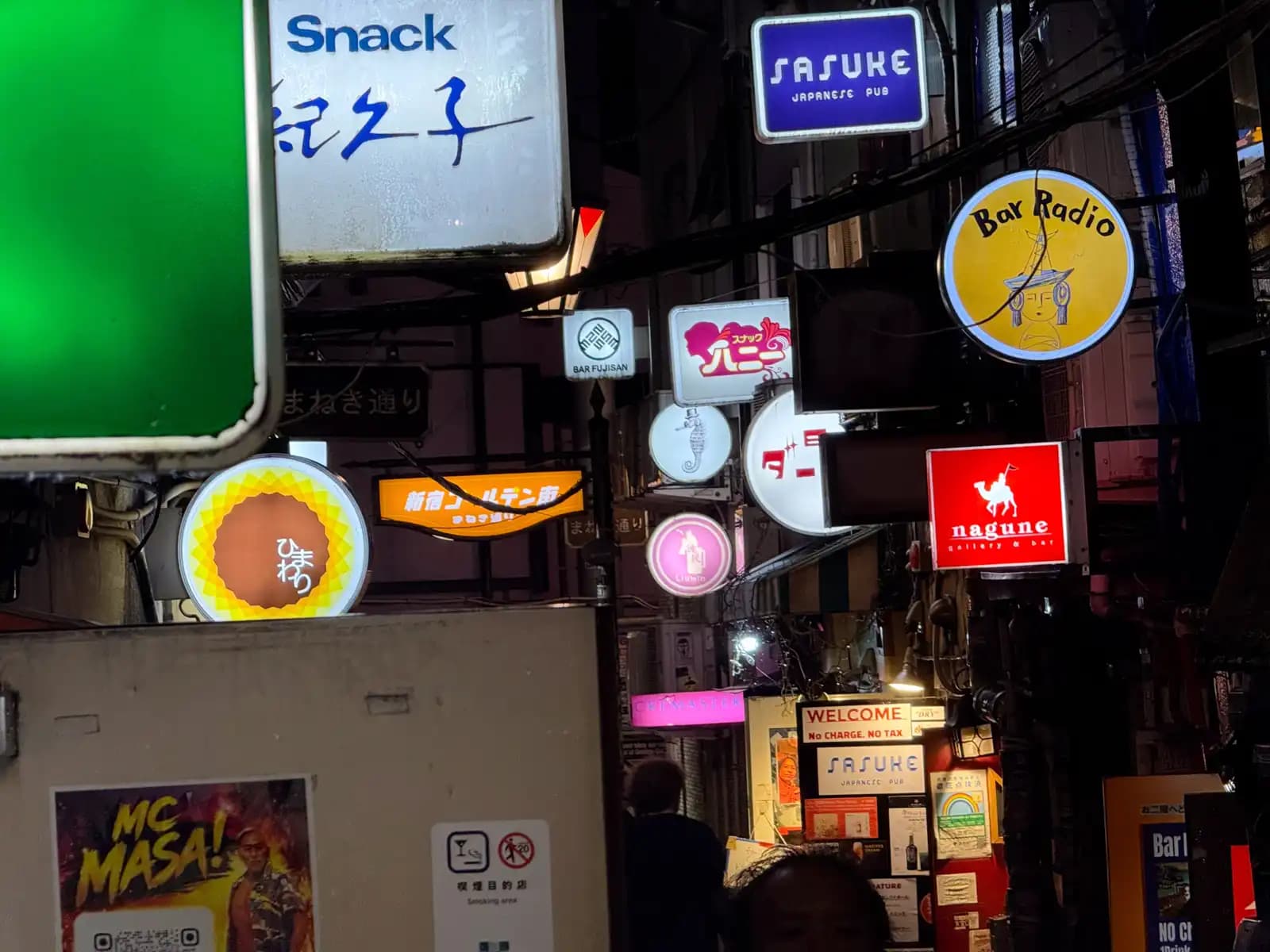 A crowd of lit-up bar signs over one alley: Snack Kikuko, Sasuke Japanese Pub, Bar Radio, Nagune and Himawari.