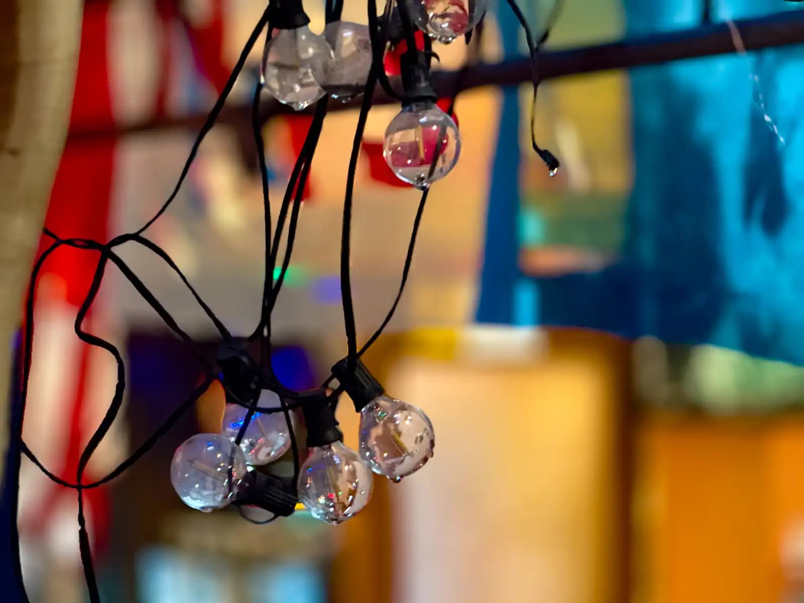 Close-up of a string of clear bulbs hanging from a bar awning, with raindrops on the glass.