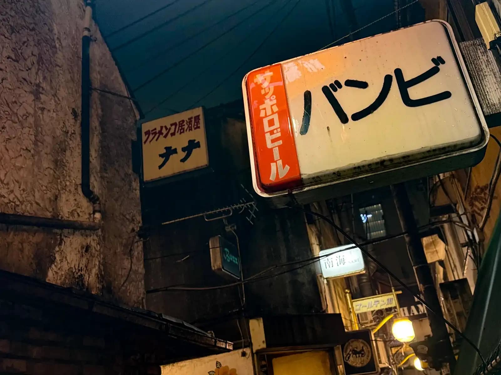 Looking up at old signs for Bambi with a Sapporo Beer logo and the flamenco izakaya Nana.