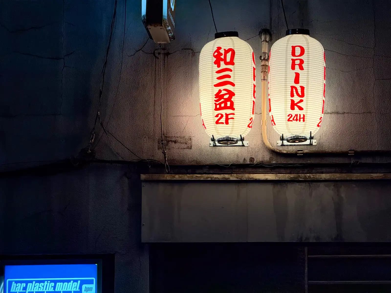 Two paper lanterns on a dark wall, one for Wasanbon on the second floor and one saying "Drink 24H".