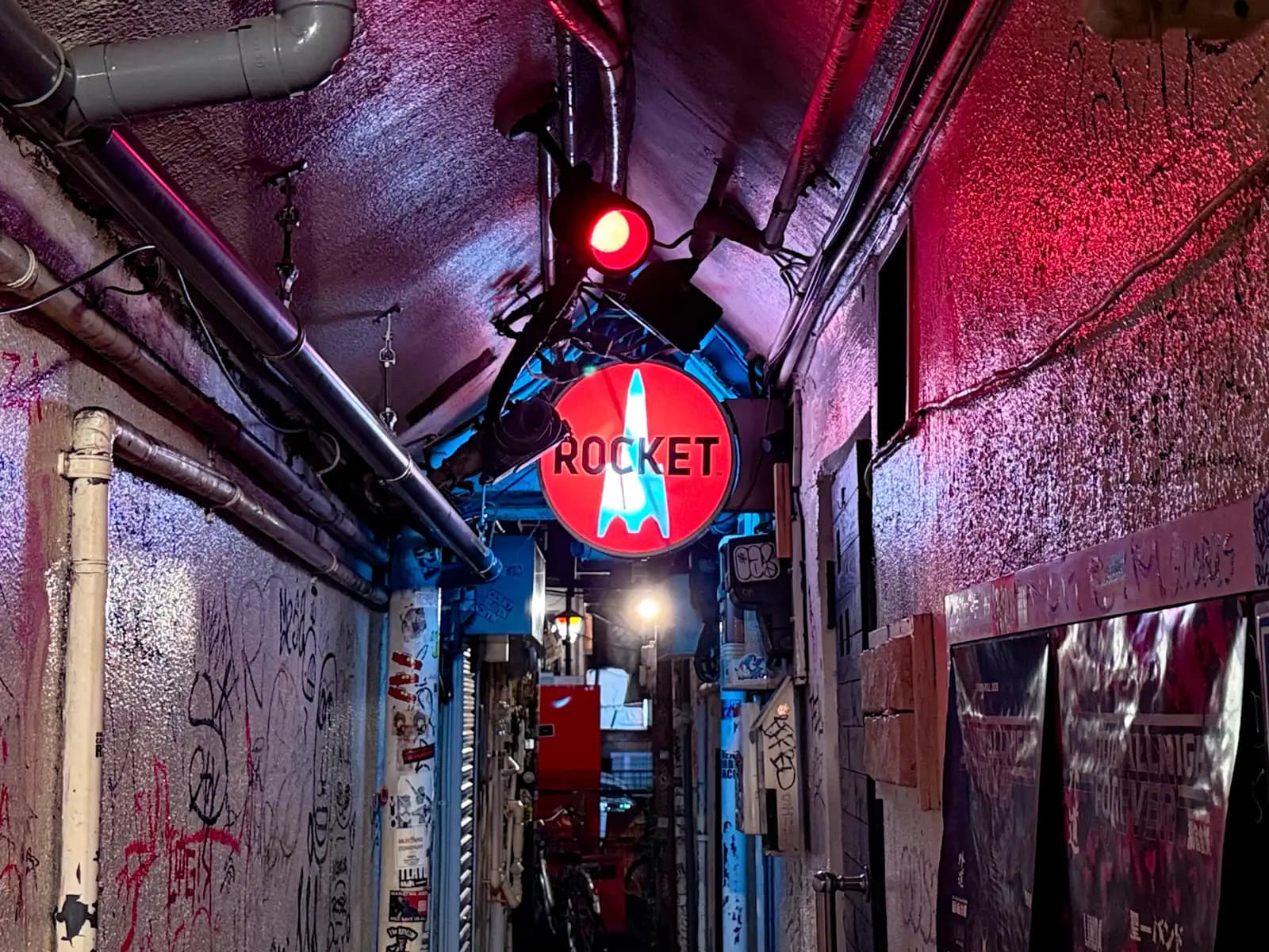 The round red Rocket sign hanging in a low covered passage, with graffiti on the walls and pipes along the ceiling.